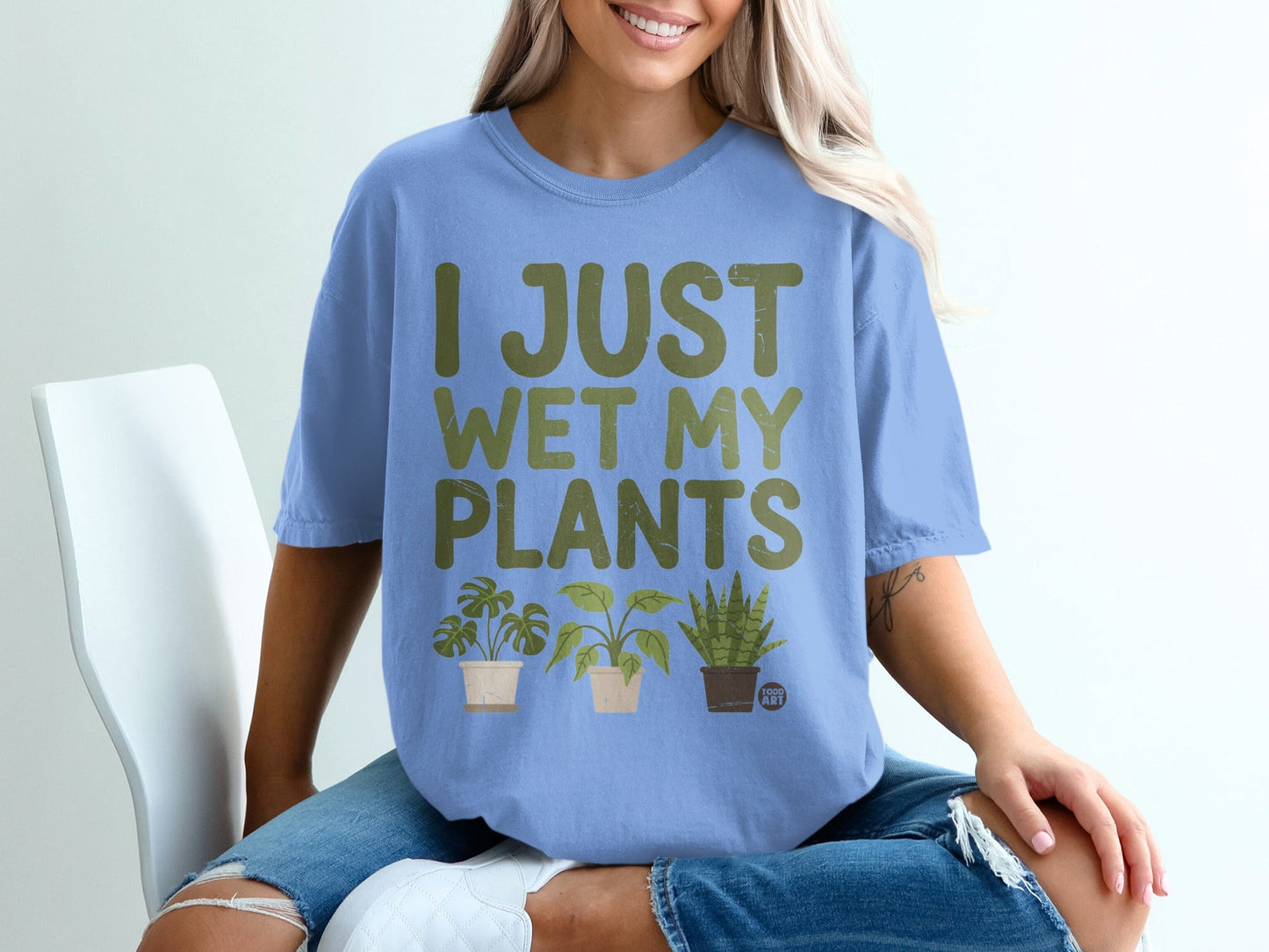 Blue t-shirt with green text "I JUST WET MY PLANTS" and three potted plants.