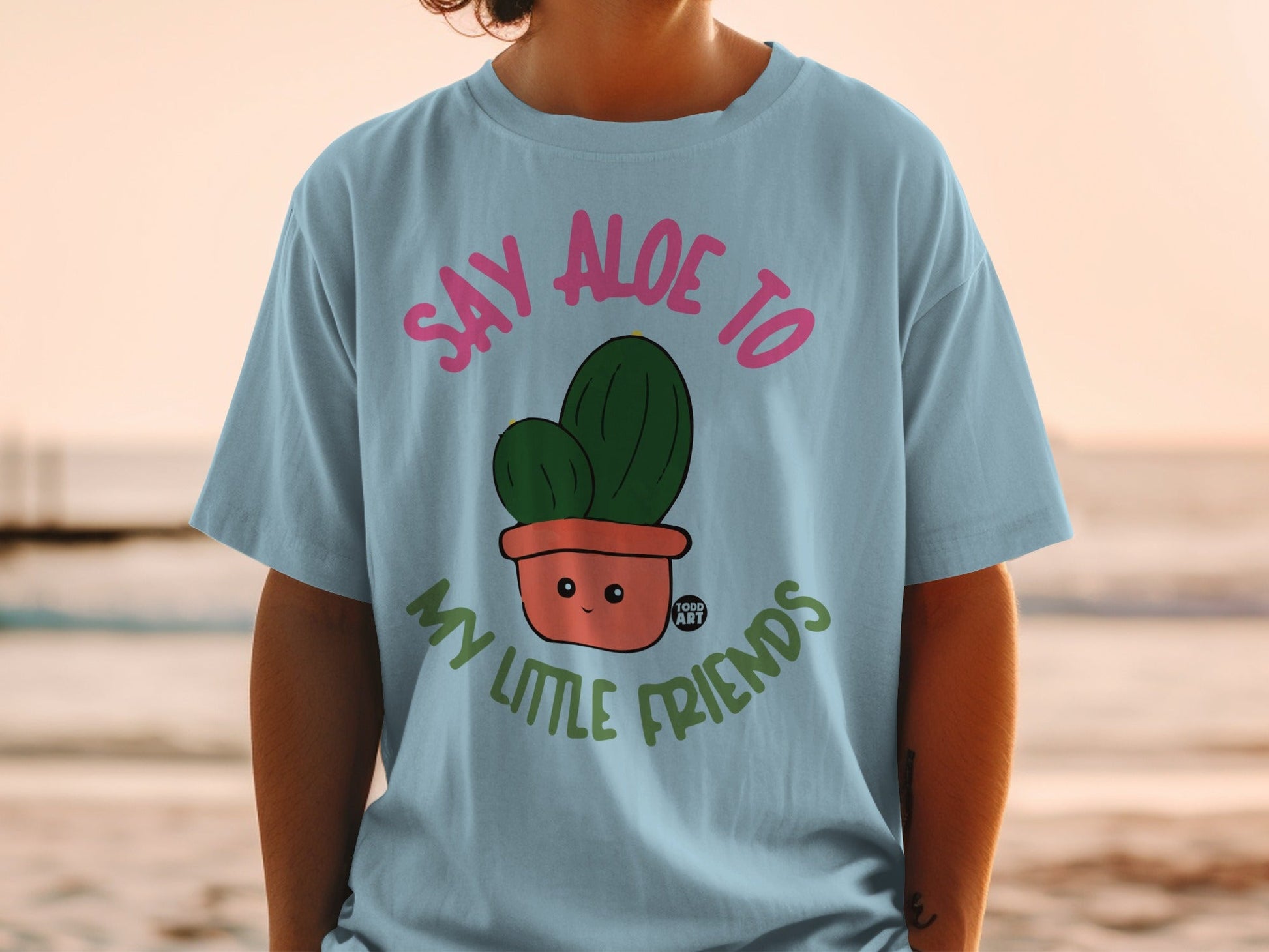 Light blue t-shirt with cartoon cactus saying "Say Aloe to My Little Friends."