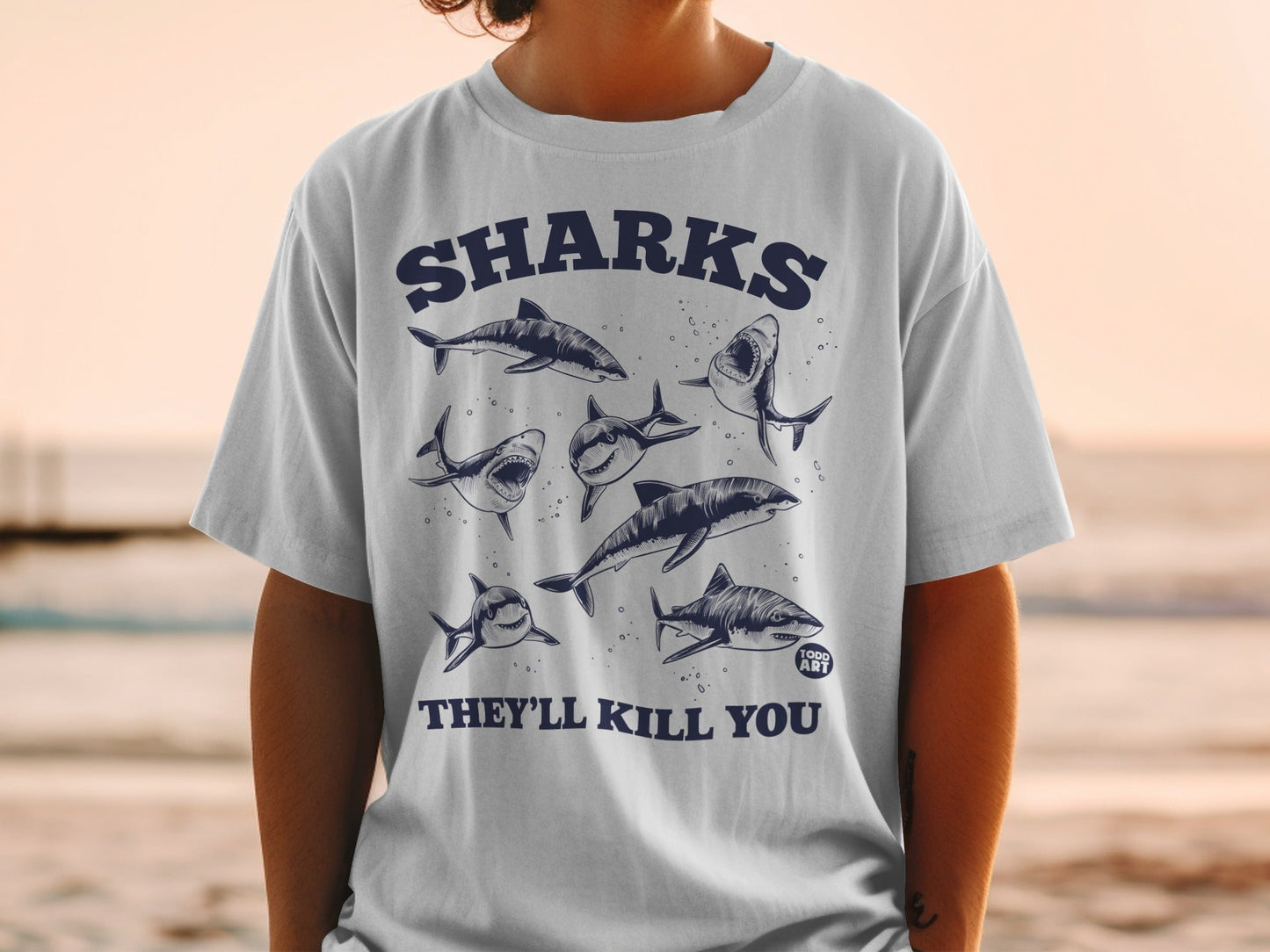 White t-shirt with cartoon sharks and text "SHARKS THEY'LL KILL YOU".