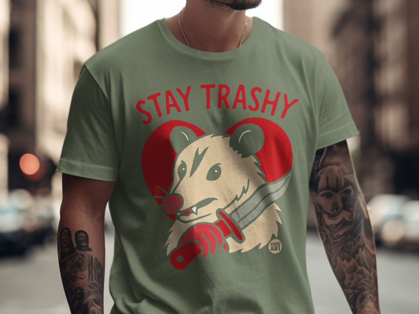 Opossum wearing shirt, holding knife, with red heart and "STAY TRASHY" text.