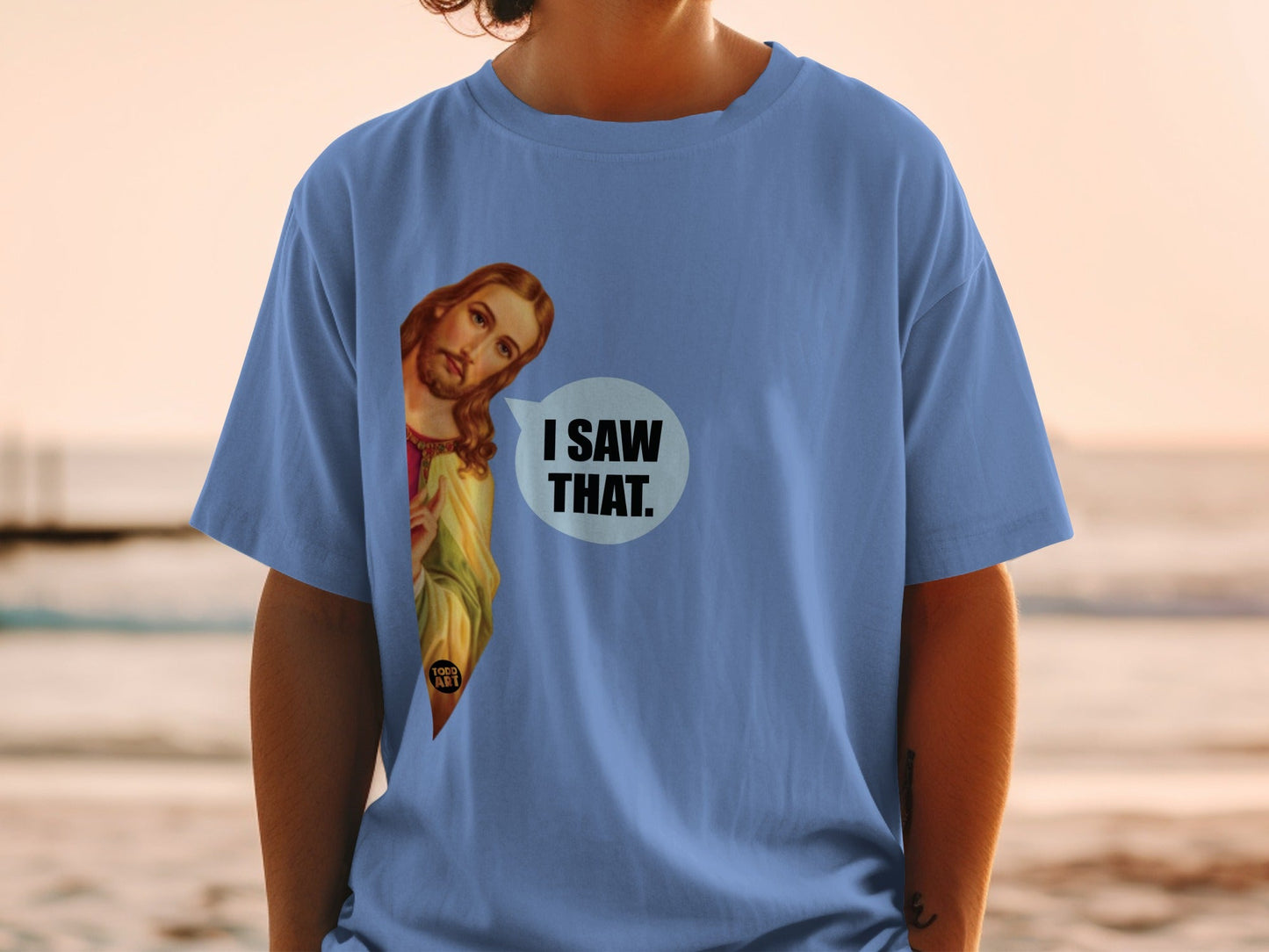 Jesus peeking from behind a blue t-shirt with "I SAW THAT." text.