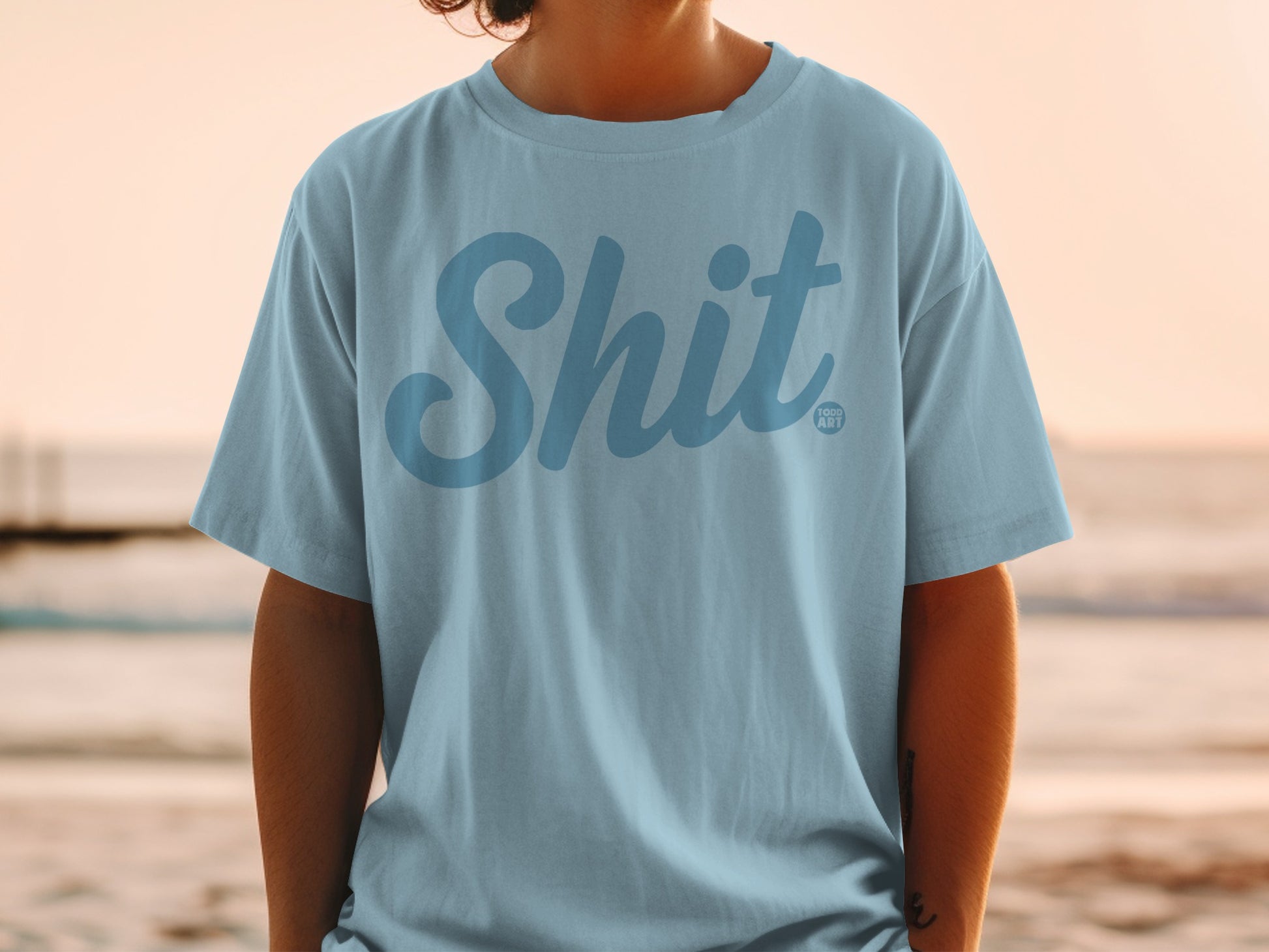 Light blue t-shirt with "Shit" and "GOOD ART" logo in blue text.