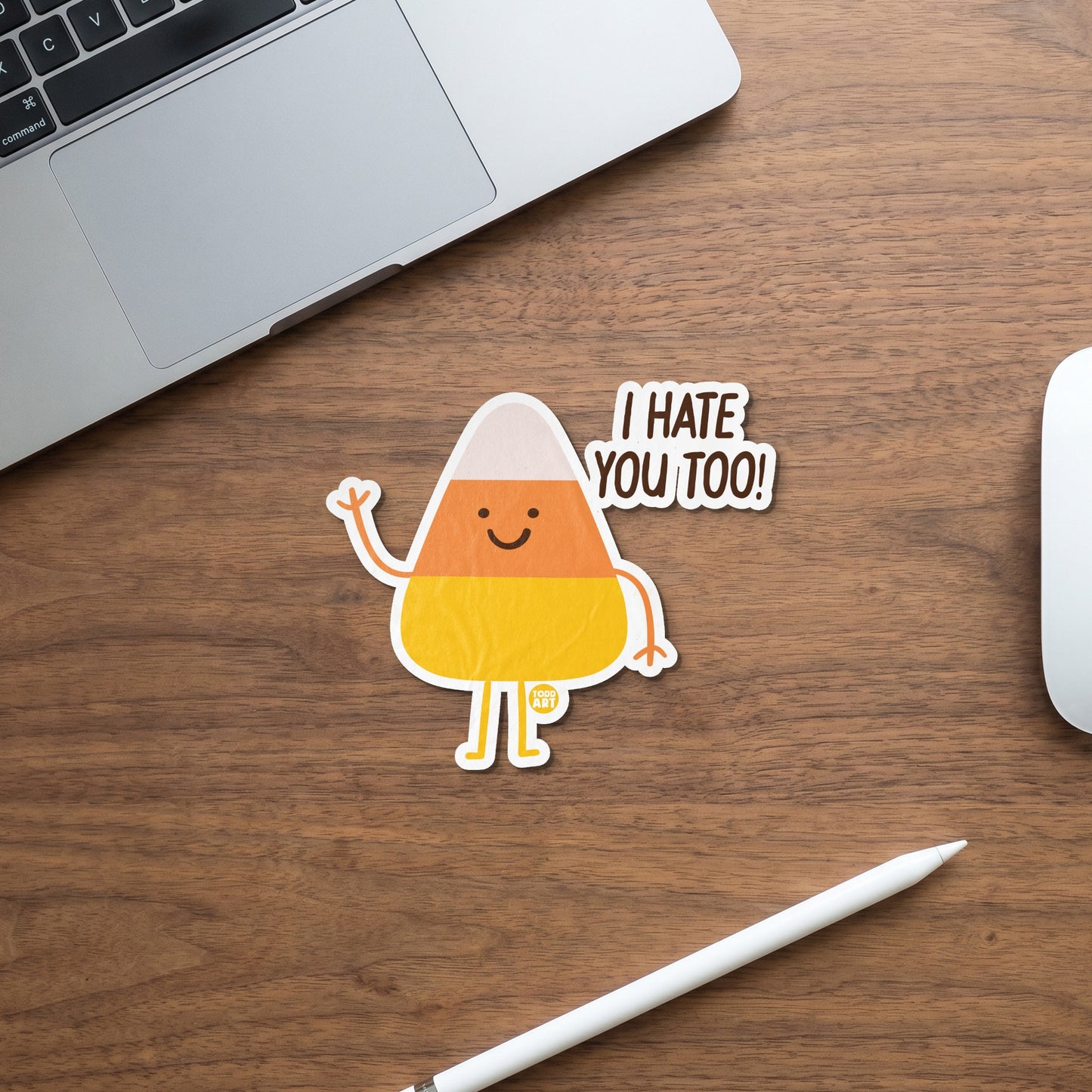 Candy corn sticker with "I hate you too!" text on a wooden desk.
