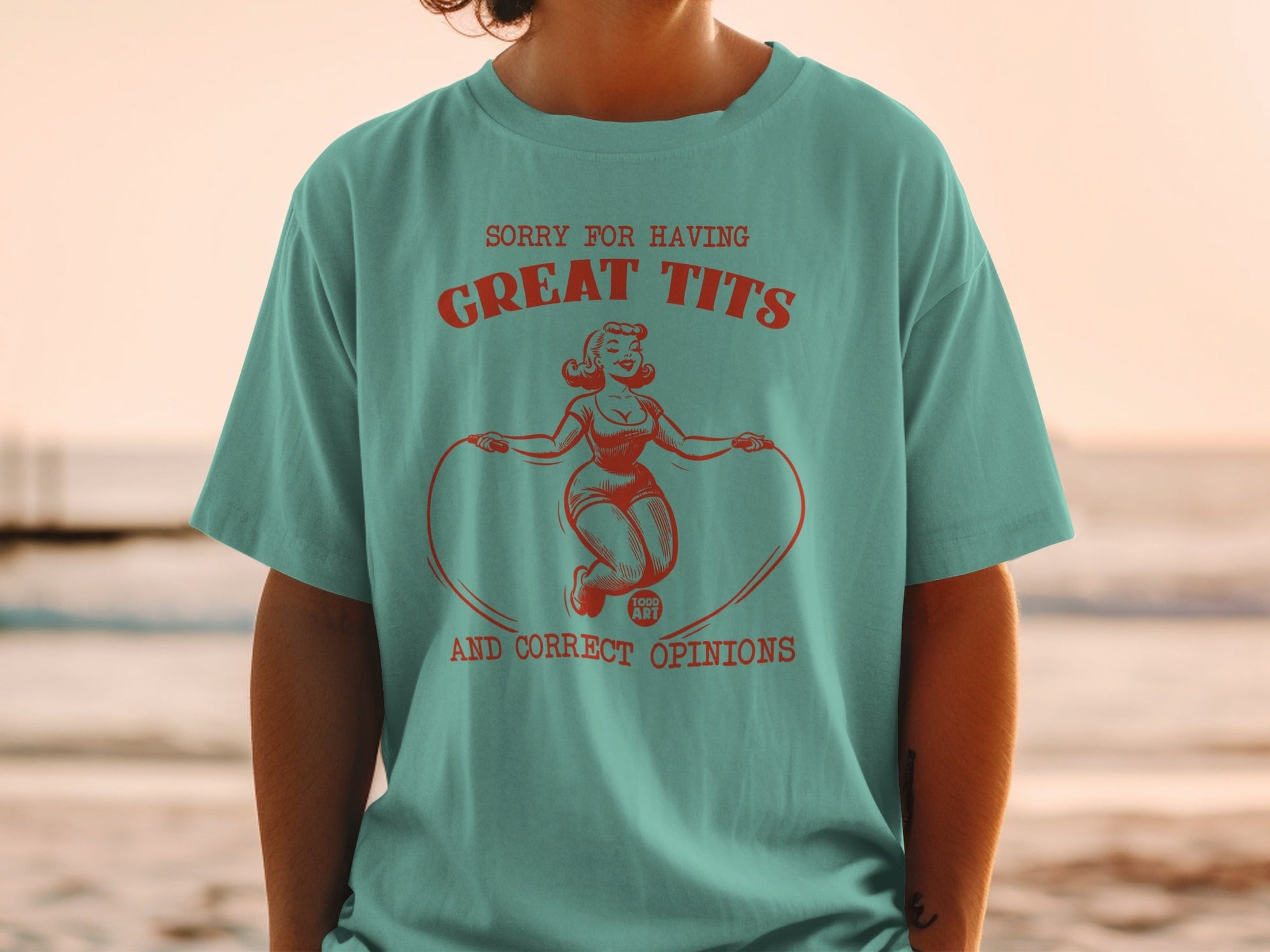Turquoise t-shirt with red graphic of woman jumping rope, "SORRY FOR HAVING GREAT TITS AND CORRECT OPINIONS".