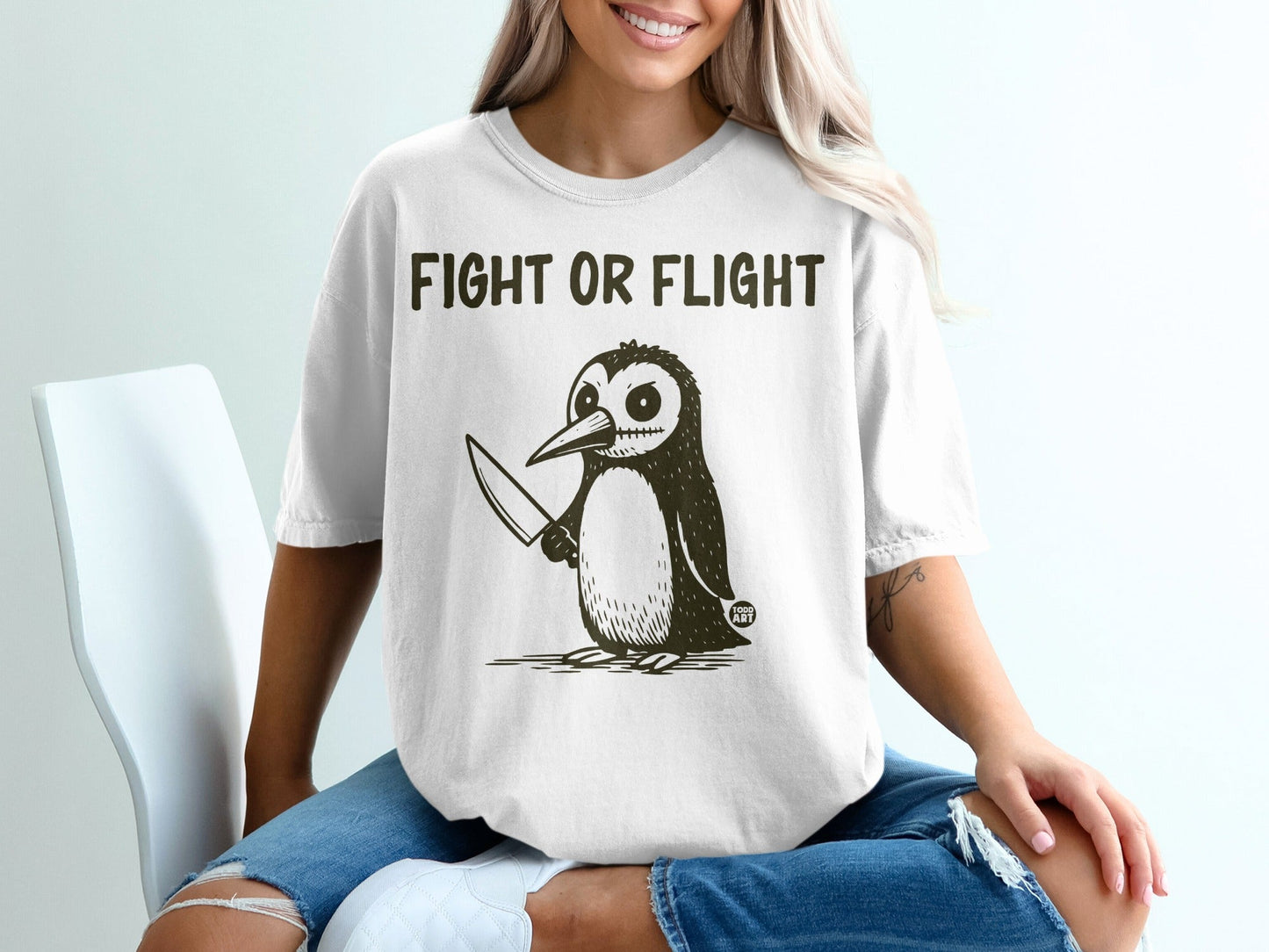 Cartoon penguin with knife and text "FIGHT OR FLIGHT" on white t-shirt.