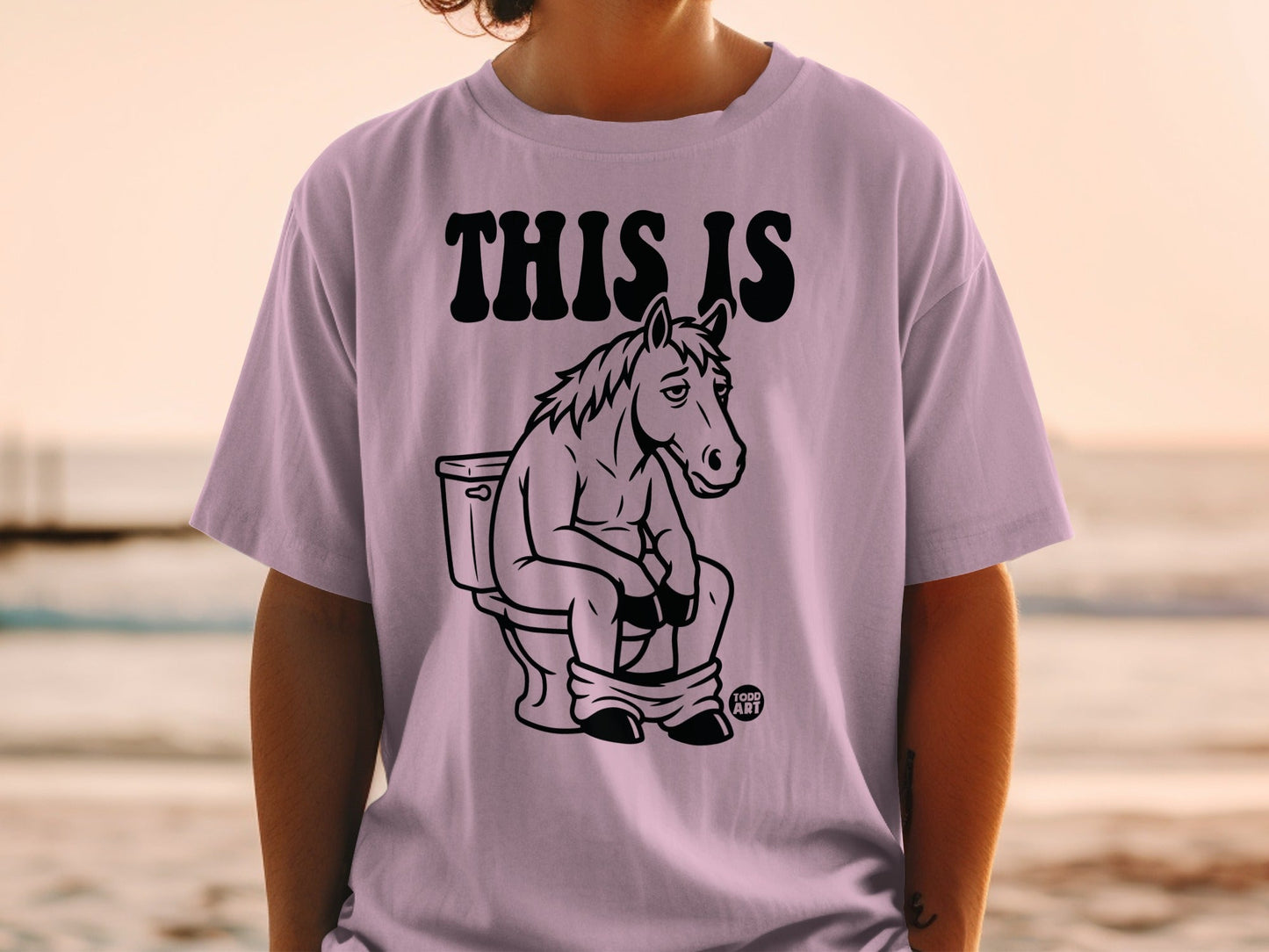T-shirt with "THIS IS" text and a cartoon horse sitting on a toilet.