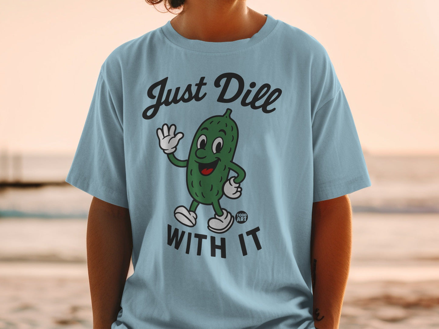 Light blue t-shirt with cartoon pickle saying "Just Dill With It".