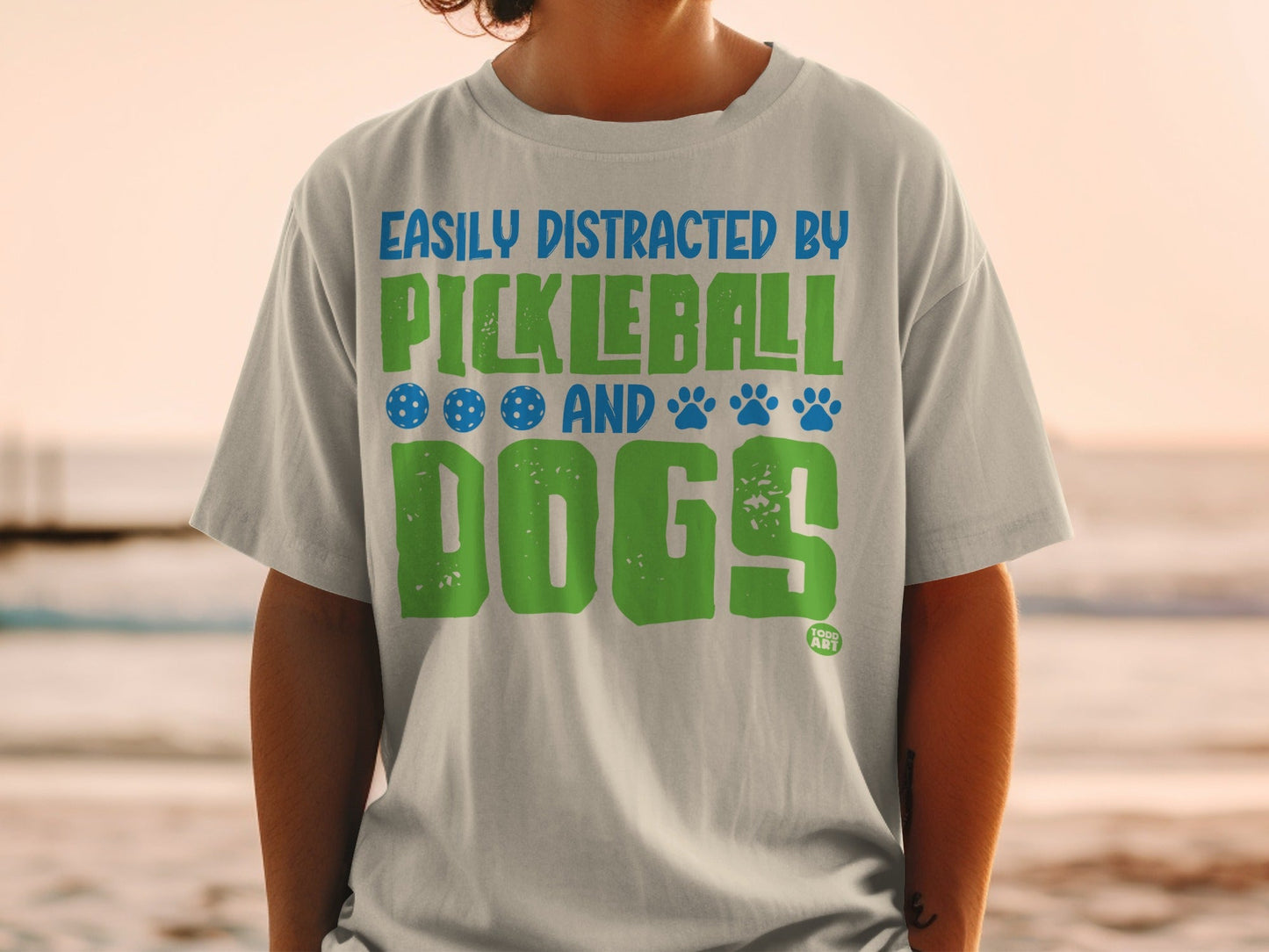 Light gray t-shirt with "Easily Distracted By Pickleball And Dogs" text and icons.