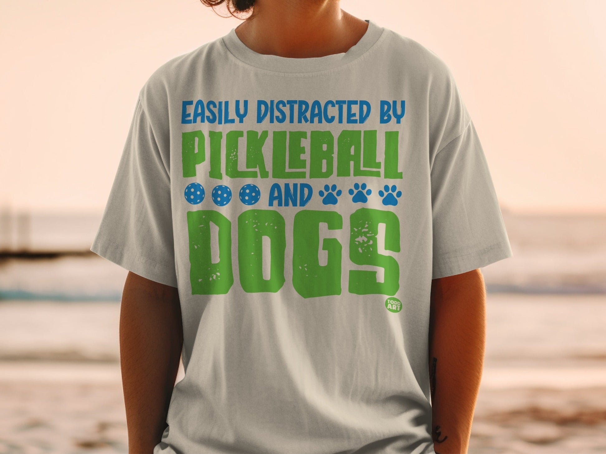 Light gray t-shirt with "Easily Distracted By Pickleball And Dogs" text and icons.