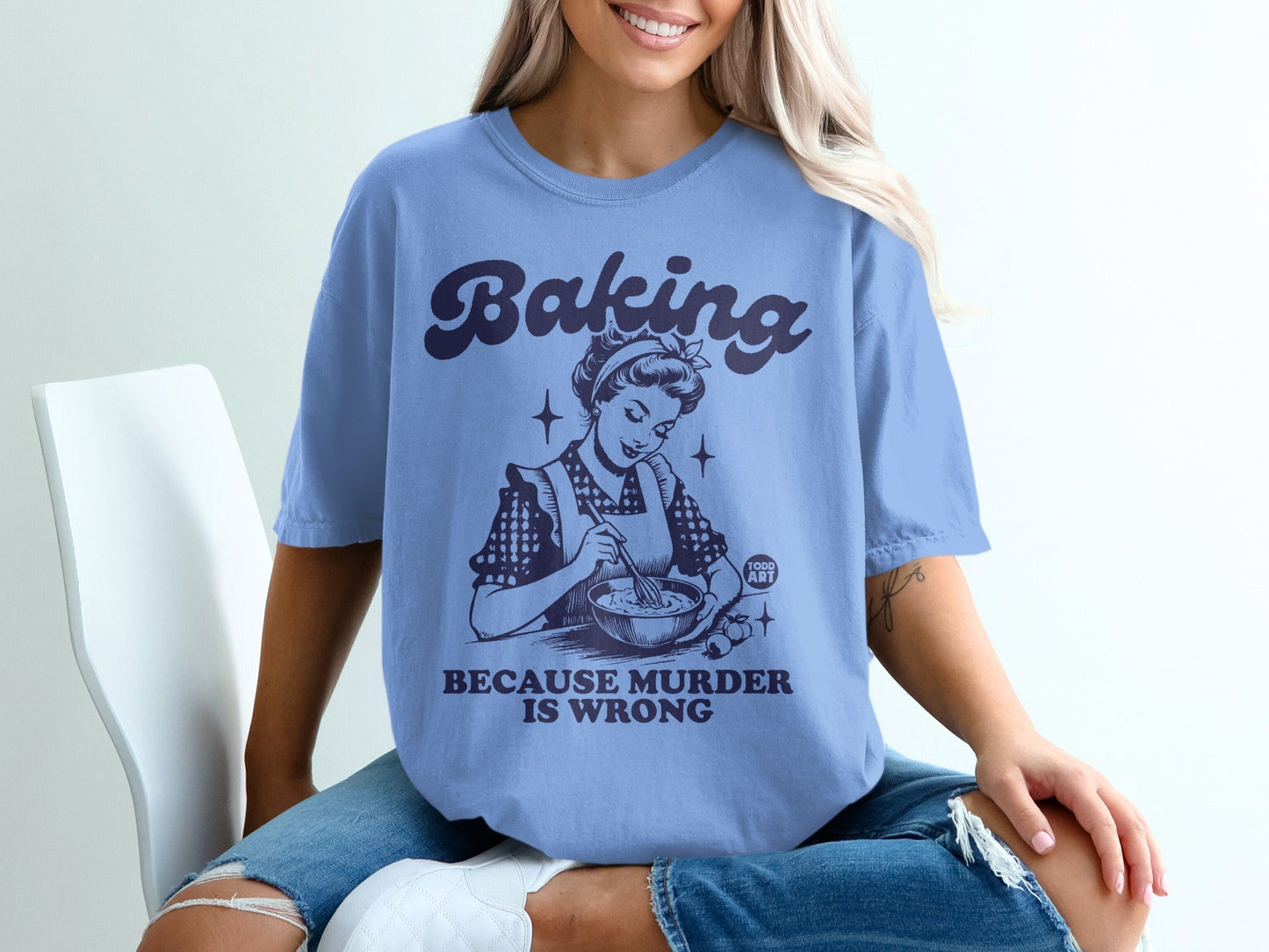 Blue t-shirt with vintage illustration of a woman baking, text "Baking Because Murder Is Wrong".