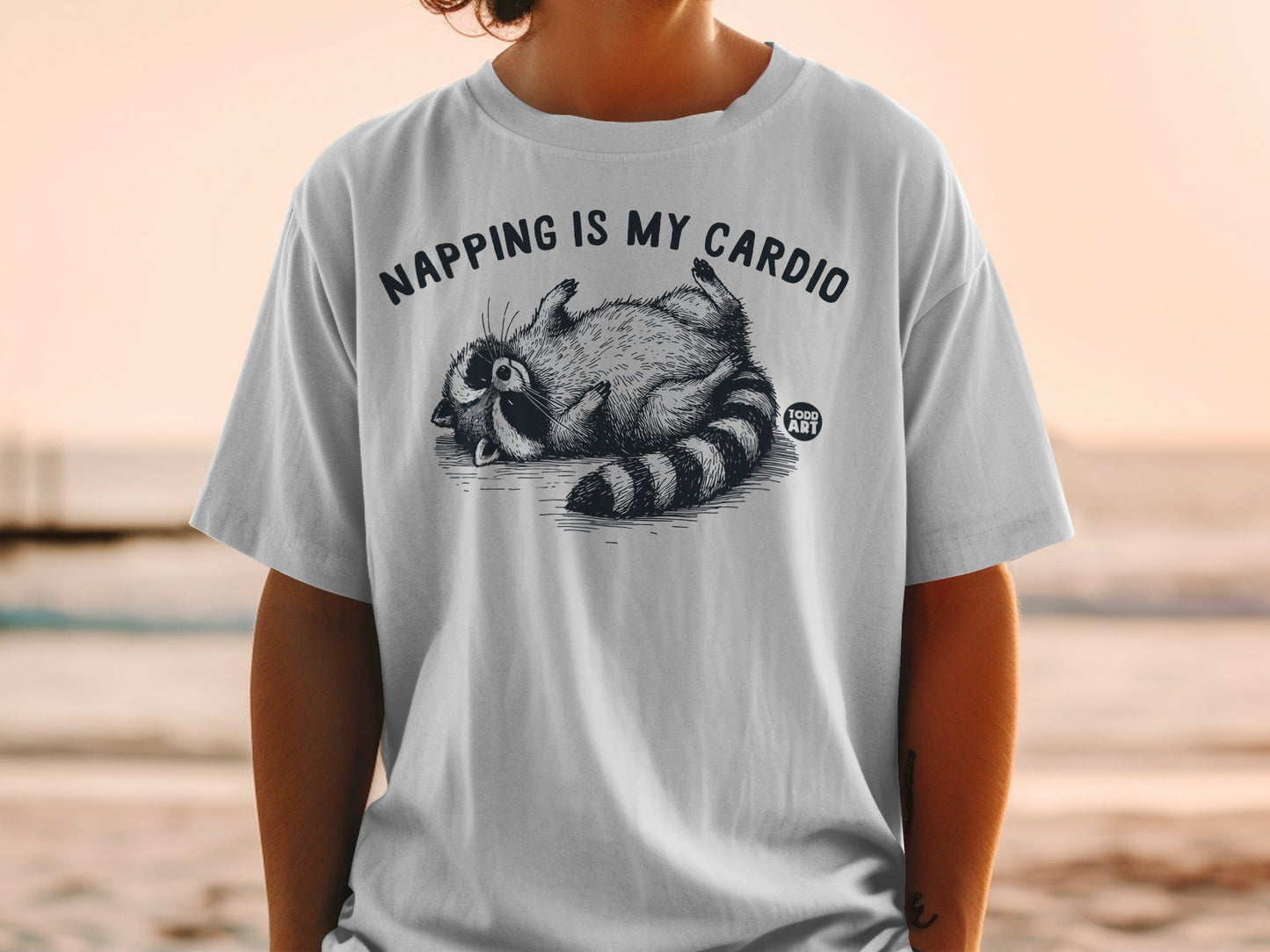 White t-shirt with raccoon graphic and "NAPPING IS MY CARDIO" text.