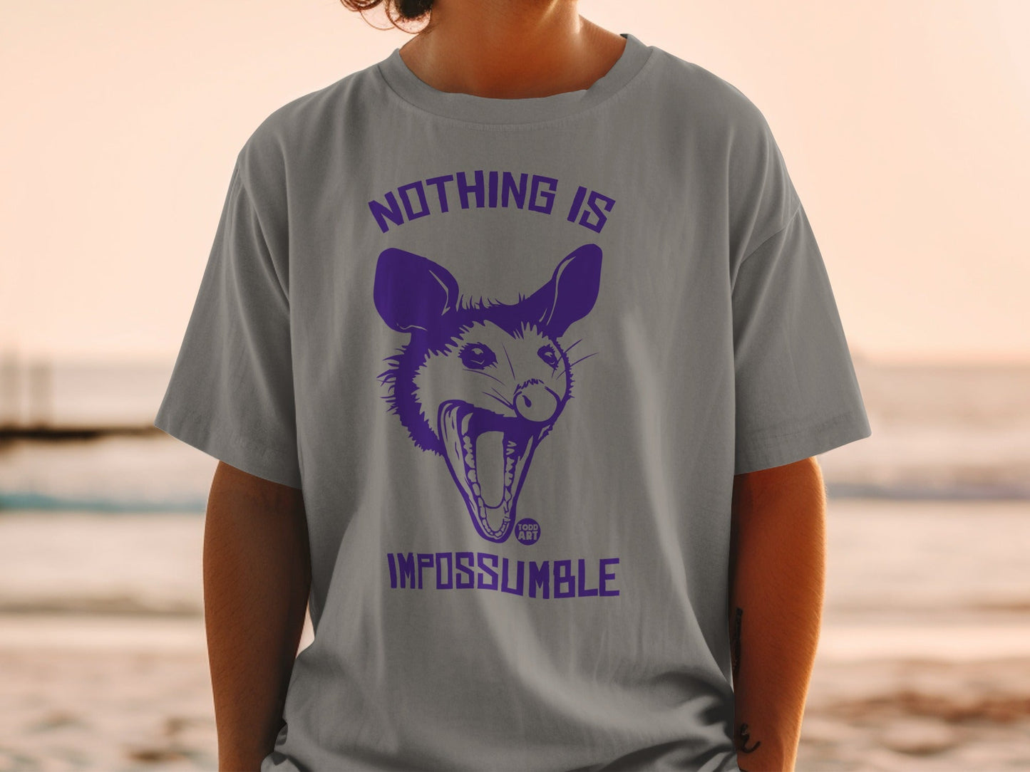 Gray t-shirt with purple graphic of a screaming opossum and text "NOTHING IS IMPOSSUMBLE".