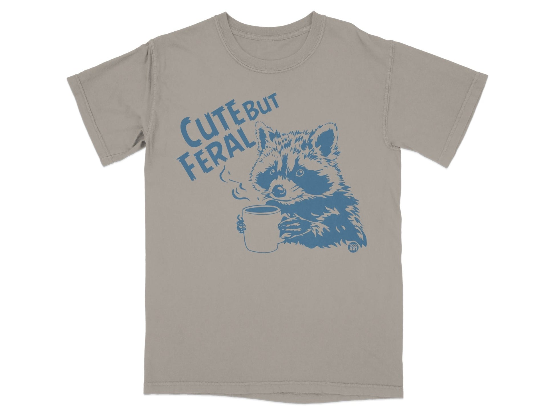 Tan t-shirt with blue raccoon holding coffee mug and text "CUTE BUT FERAL".