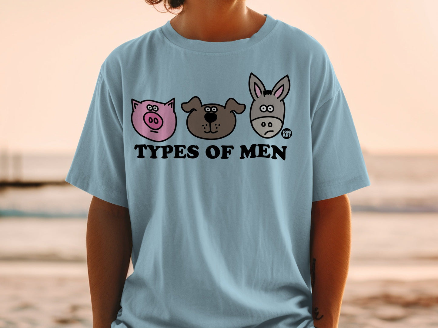 Light blue t-shirt with cartoon pig, dog, and donkey faces labeled "Types of Men".