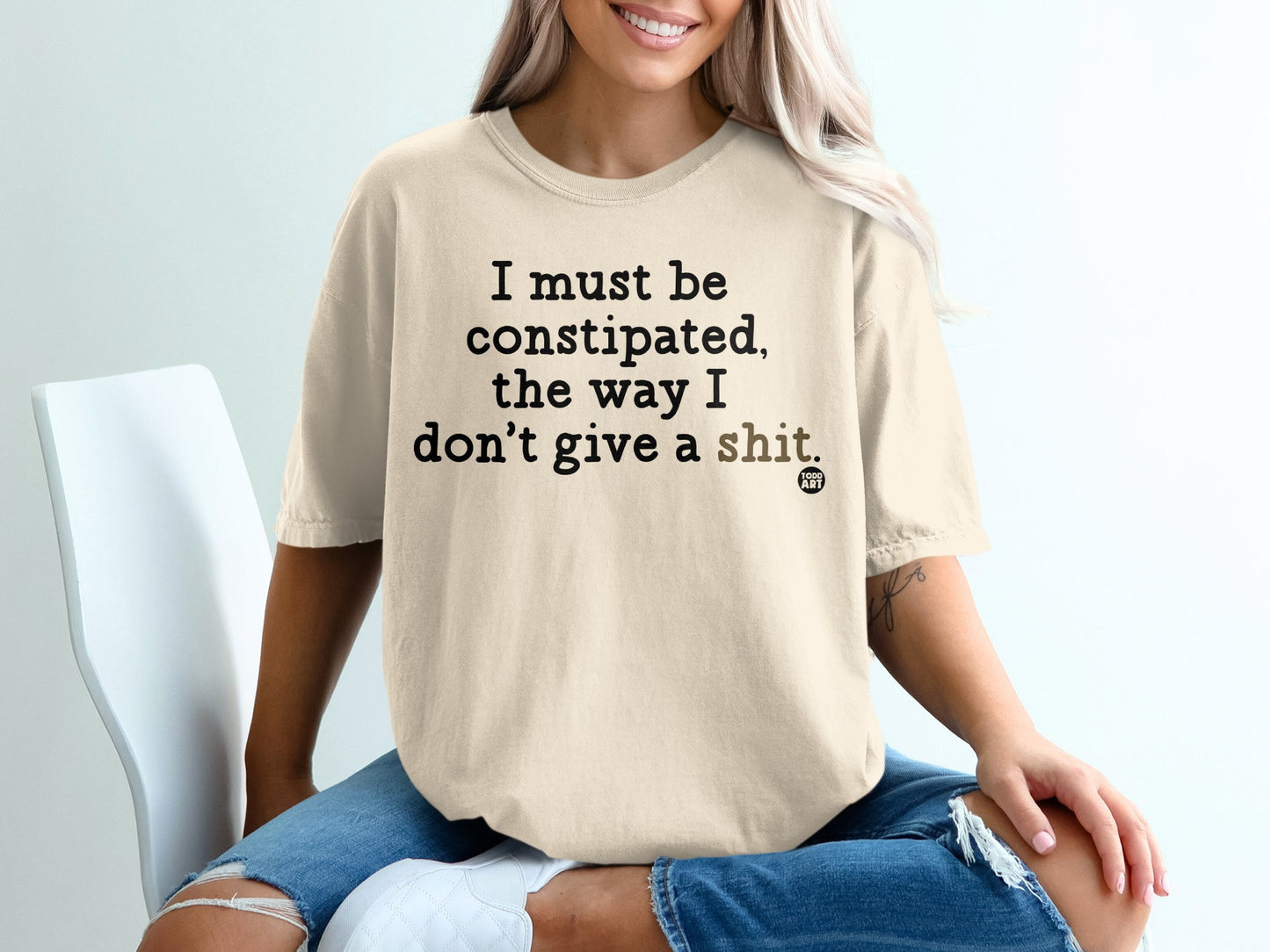 Cream t-shirt with bold black text stating "I must be constipated, the way I don't give a shit."