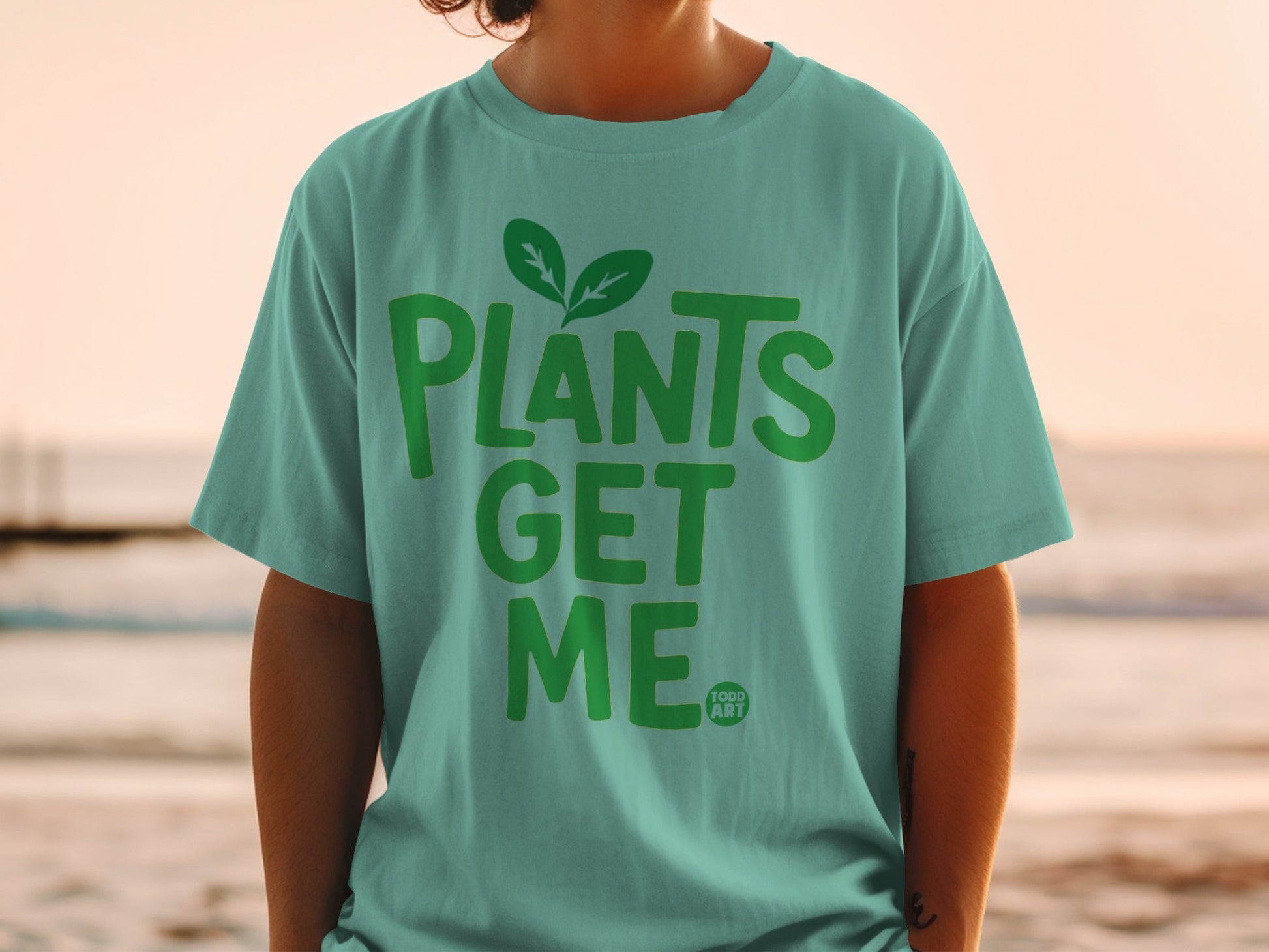Teal t-shirt with green "Plants Get Me" text and plant leaves.