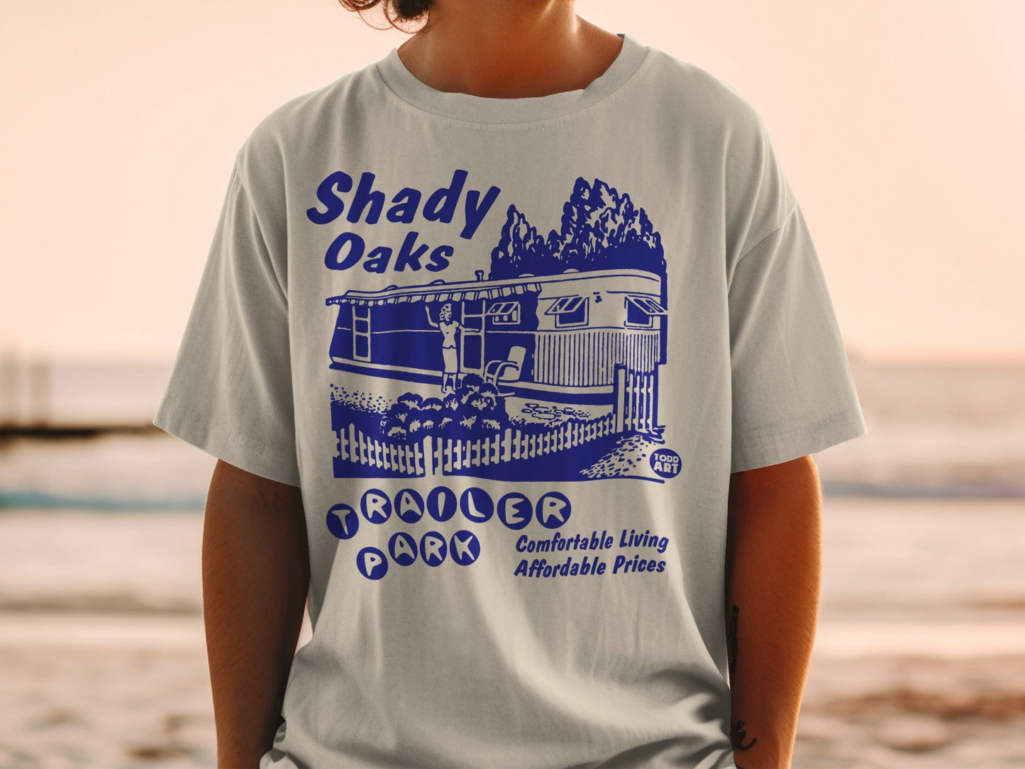 Blue t-shirt graphic with "Shady Oaks Trailer Park" text and illustration.