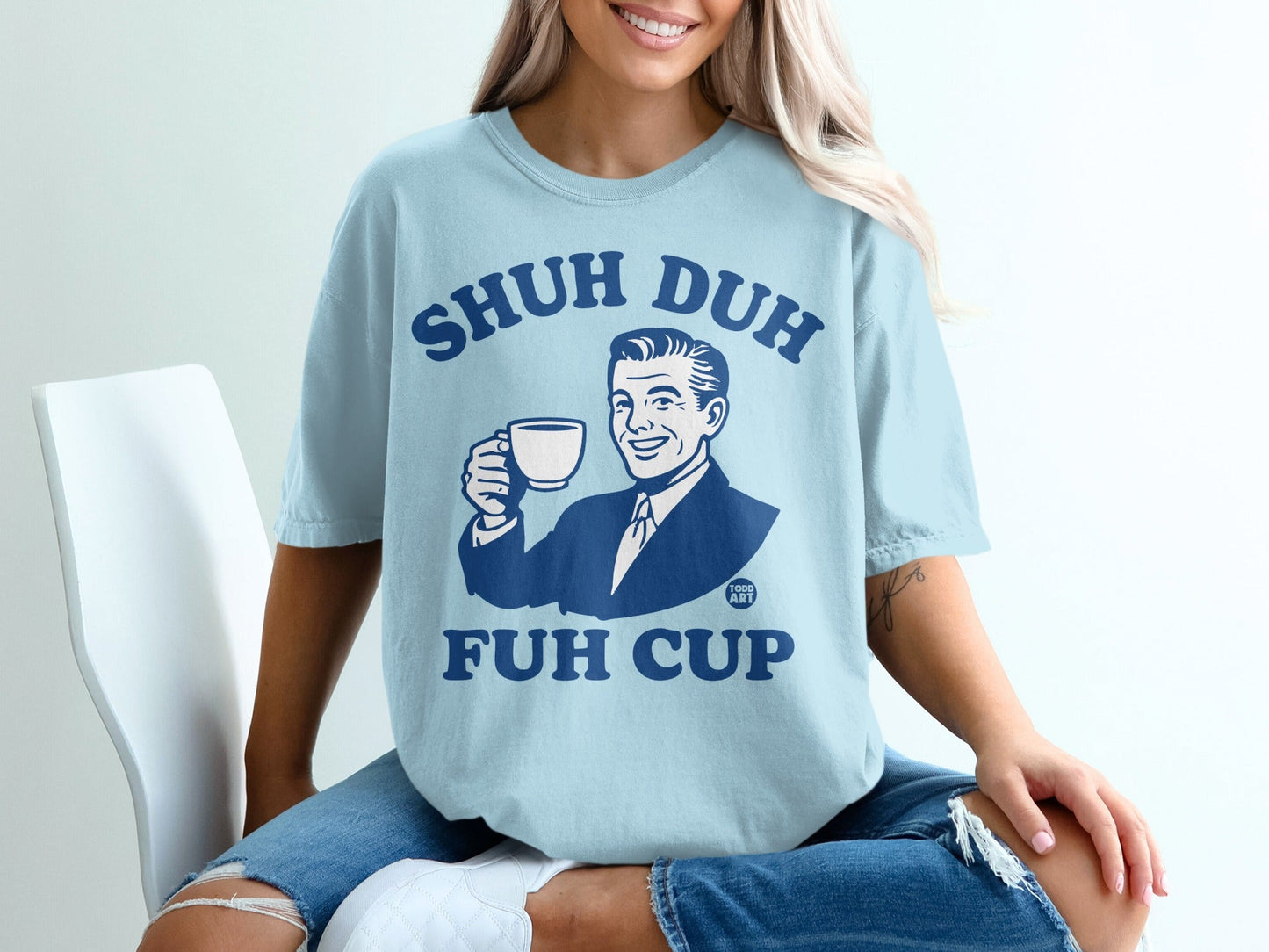 Light blue t-shirt with "Shuh Duh Fuh Cup" text and man holding coffee.