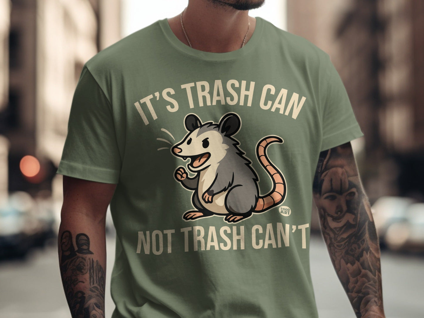Green t-shirt with cartoon possum and text "IT'S TRASH CAN NOT TRASH CAN'T".