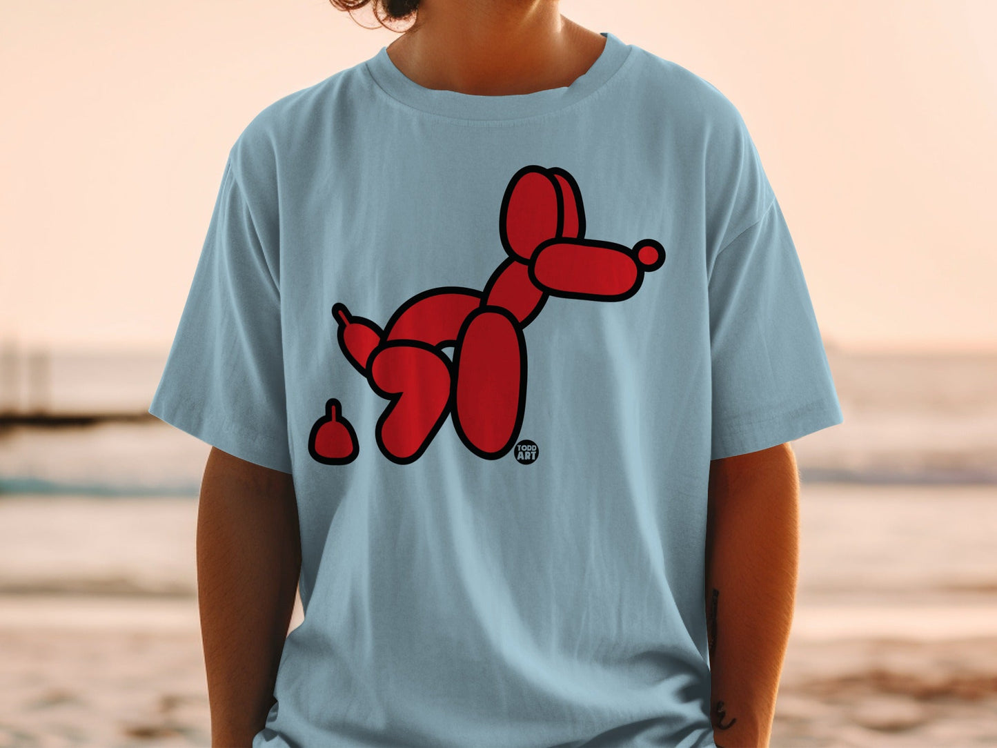 Red balloon dog with a brown poop accessory on a light blue t-shirt.
