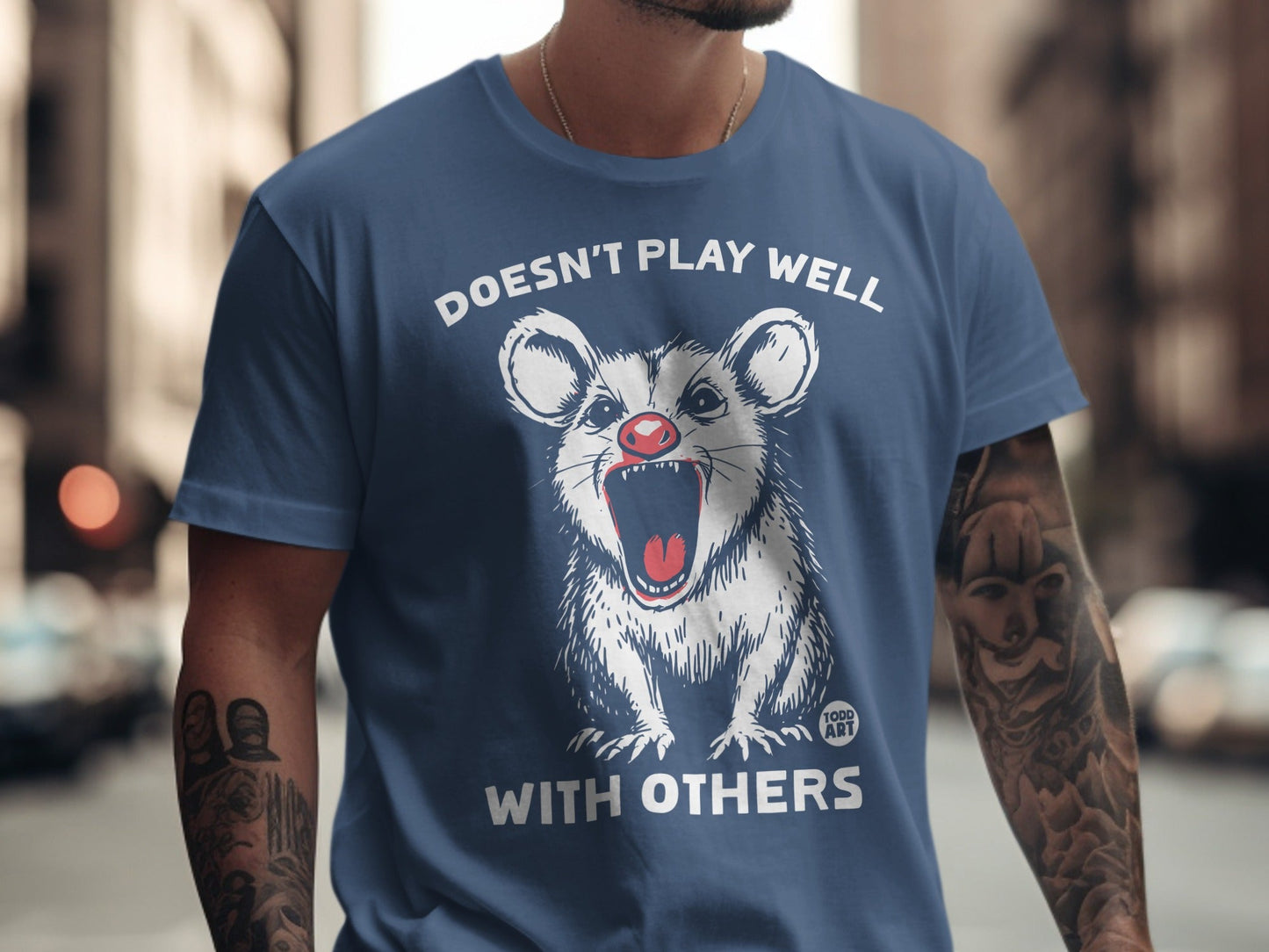 Opossum with red eyes and open mouth wearing a blue t-shirt.
