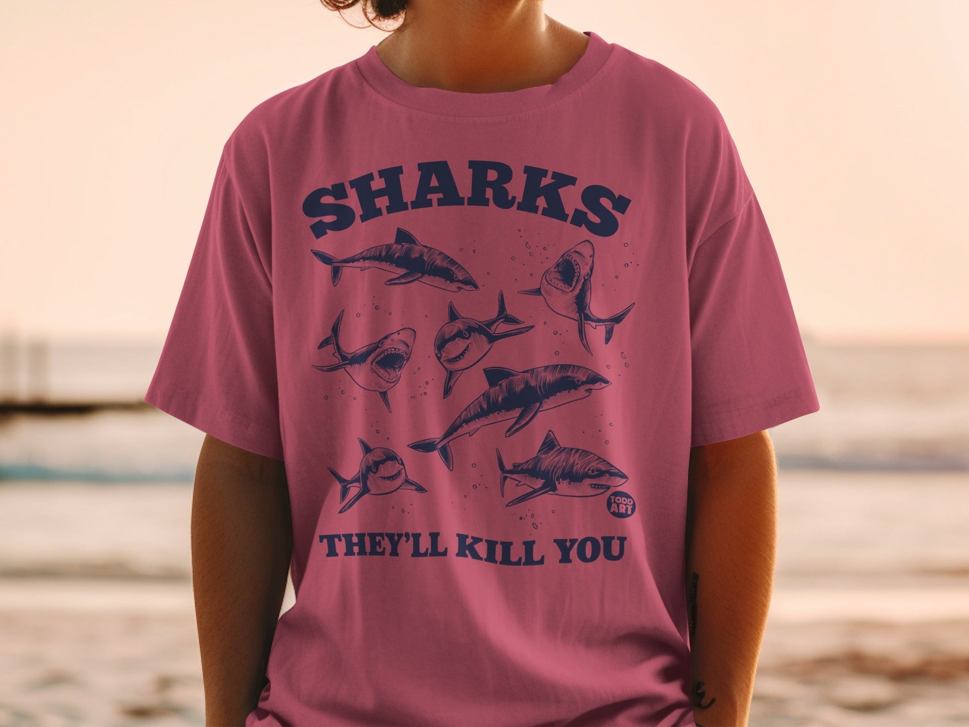 Pink t-shirt with cartoon sharks and text "SHARKS THEY'LL KILL YOU 1989 ART".
