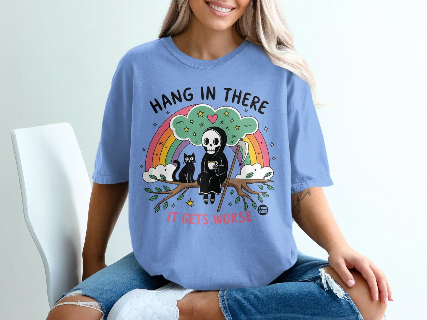 Skeleton reaper with rainbow, coffee, and cat on tree branch, "Hang in there it gets worse" text.
