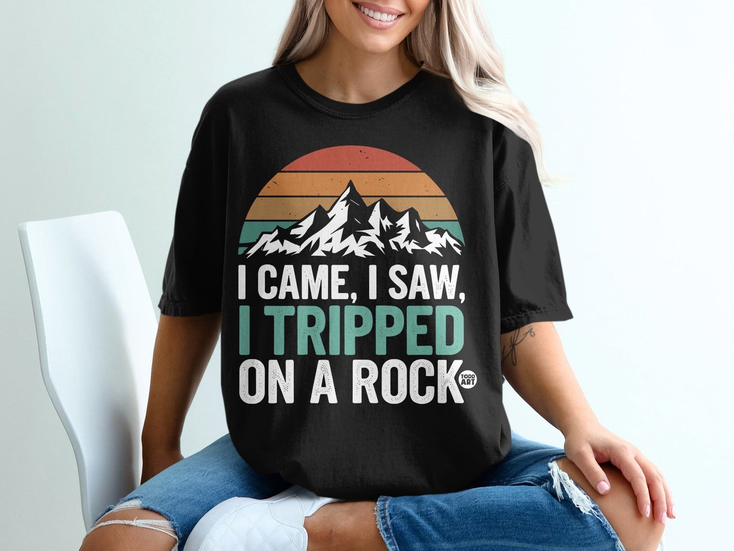 Black t-shirt with "I CAME, I SAW, I TRIPPED ON A ROCK" text and mountain graphic.