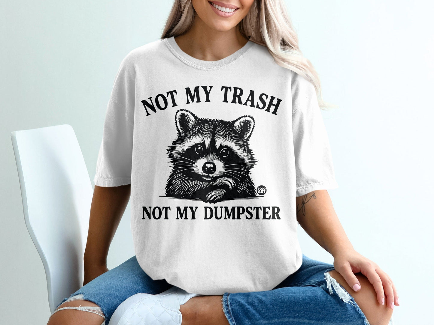 White t-shirt with a raccoon graphic and the text "NOT MY TRASH NOT MY DUMPSTER".