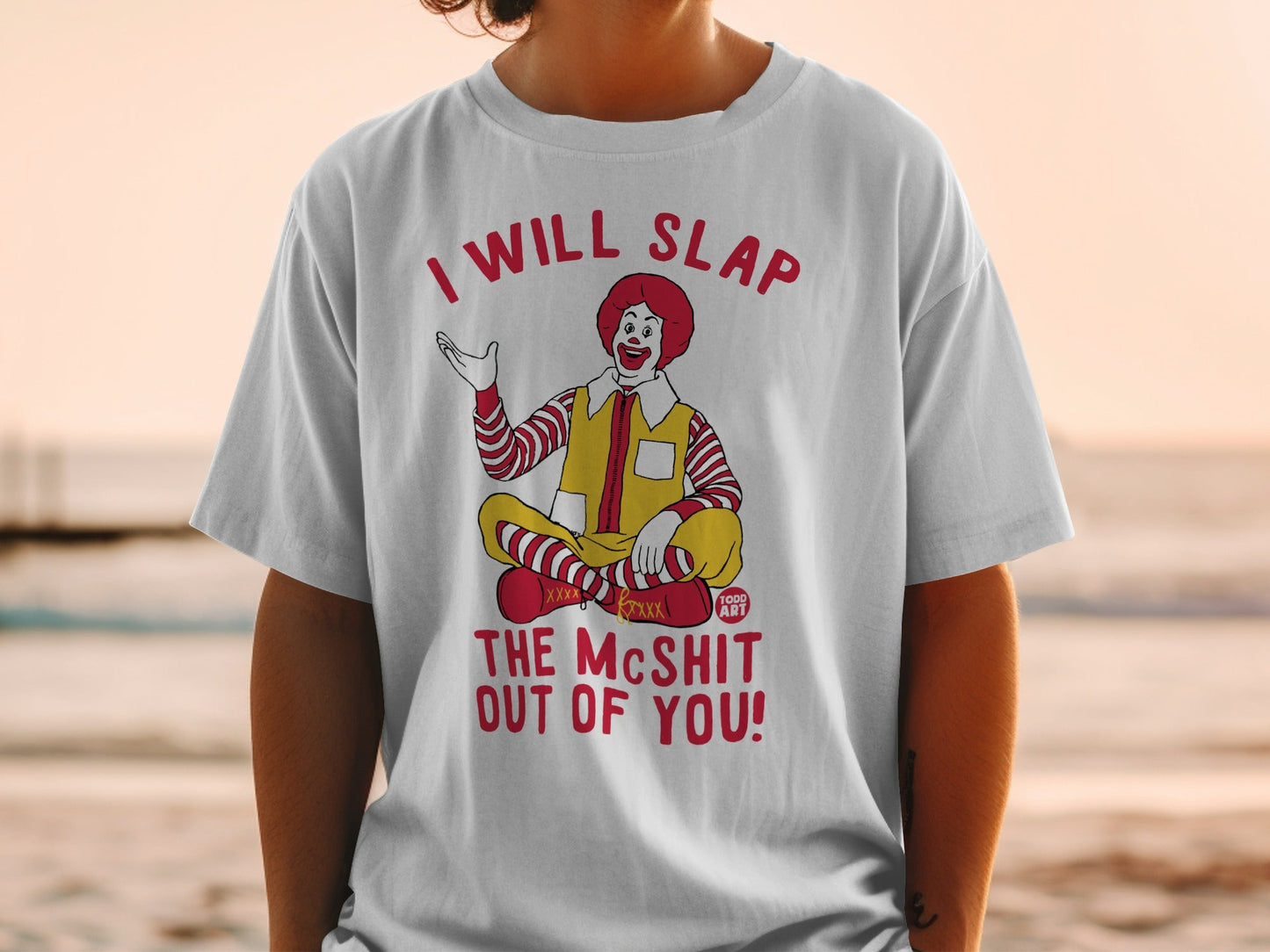Grimace-like clown sitting cross-legged on white t-shirt.