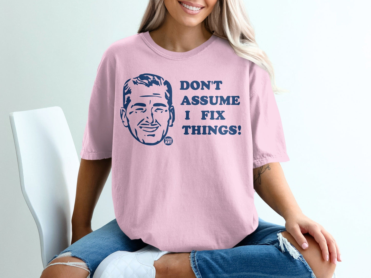 Pink t-shirt with blue text "DON'T ASSUME I FIX THINGS!" and a man's portrait.