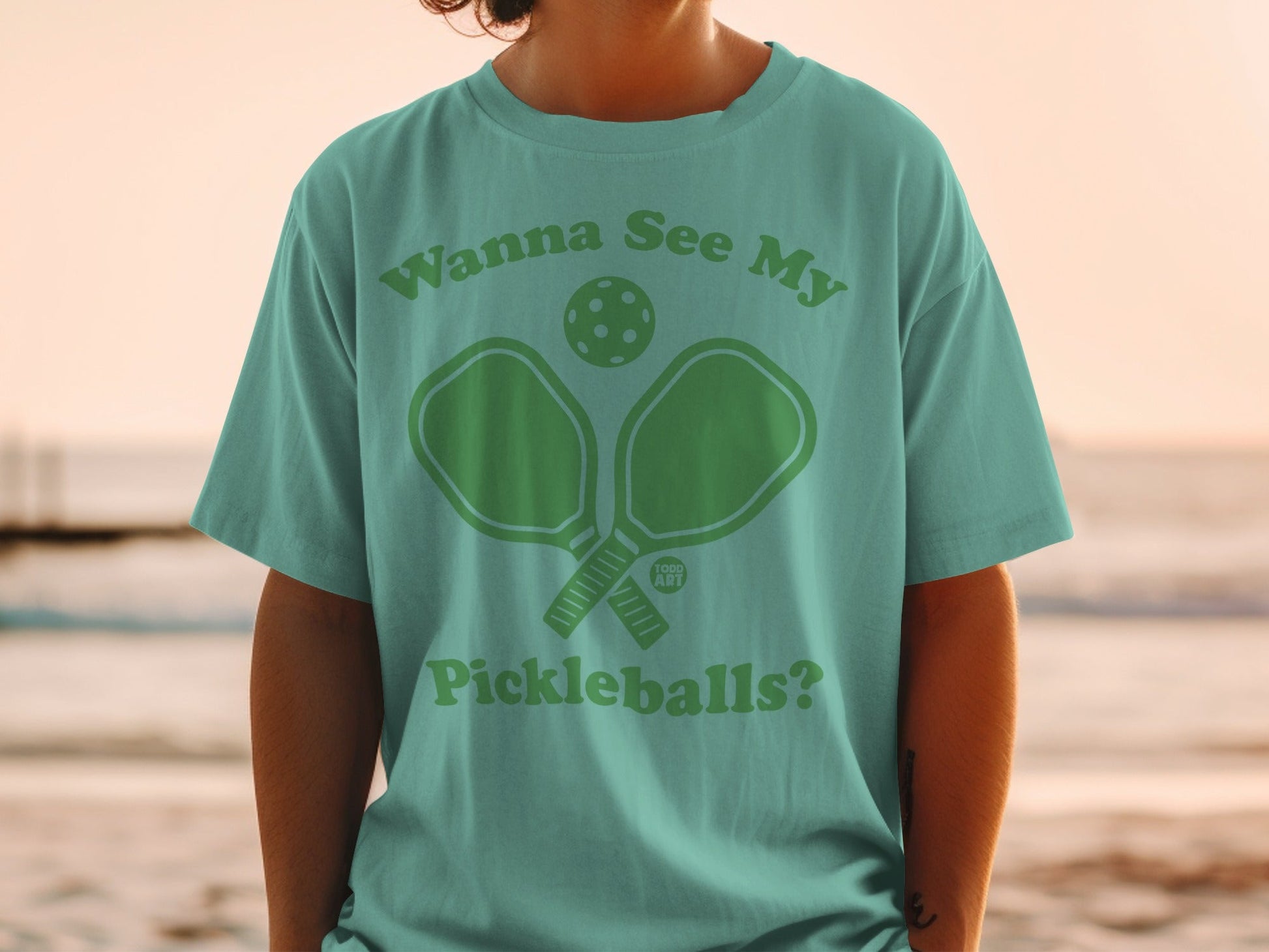 Teal t-shirt with "Wanna See My Pickleballs?" graphic and pickleball paddle.