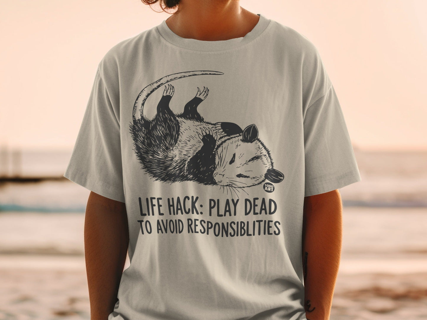 T-shirt with possum illustration and text "LIFE HACK: PLAY DEAD TO AVOID RESPONSIBILITIES".