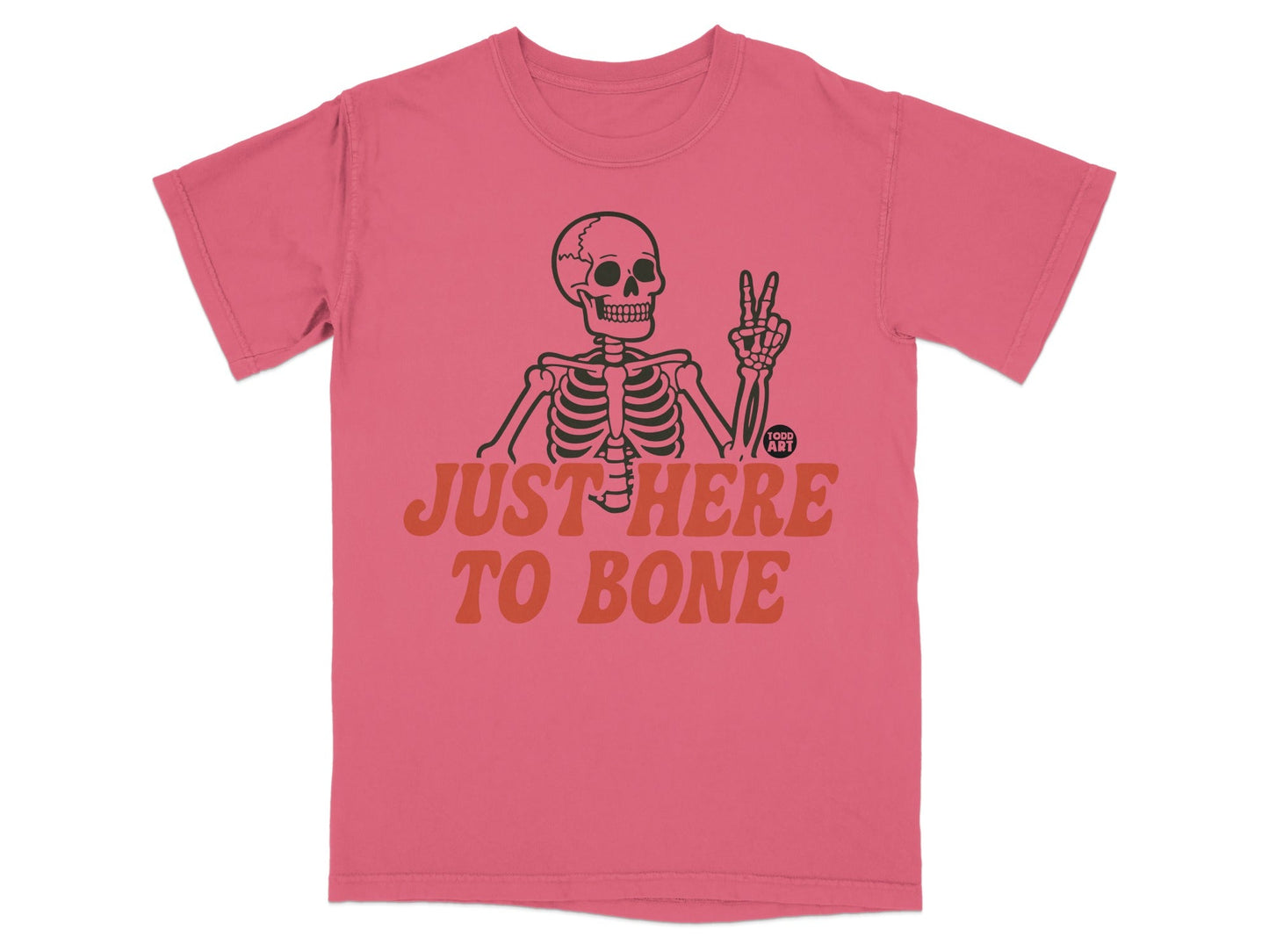 Pink t-shirt with skeleton giving peace sign and text "JUST HERE TO BONE".
