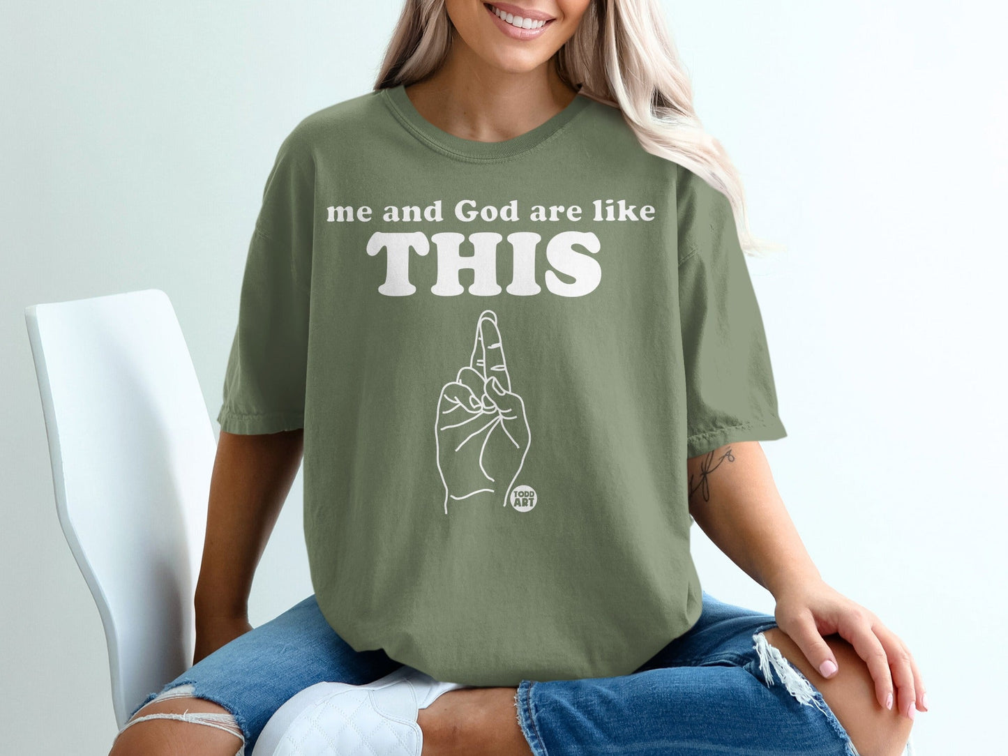 Olive green t-shirt with "me and God are like THIS" and hand gesture.
