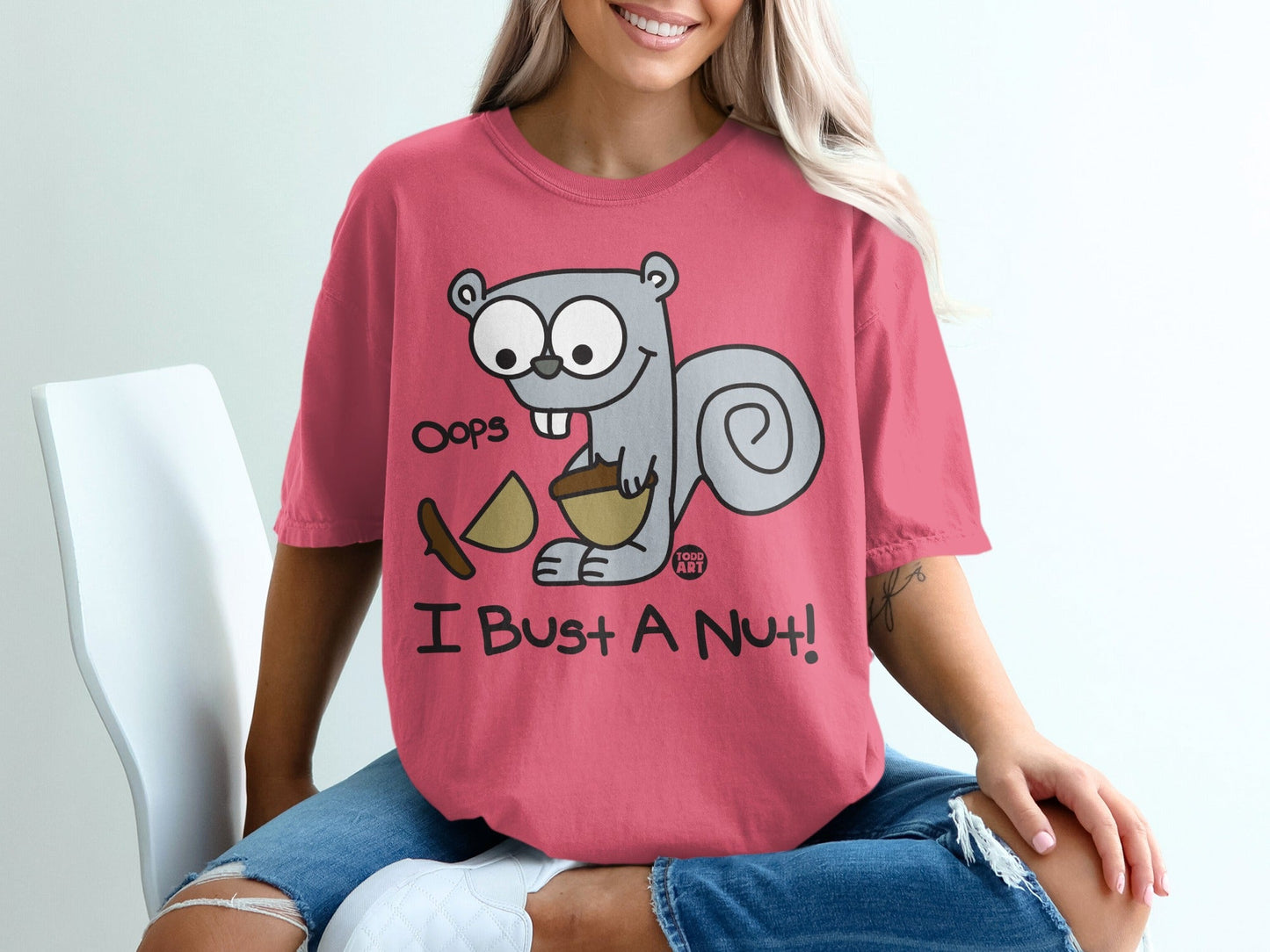 Pink t-shirt with a cartoon squirrel holding a nut and acorns, "Oops I Bust A Nut!" text.