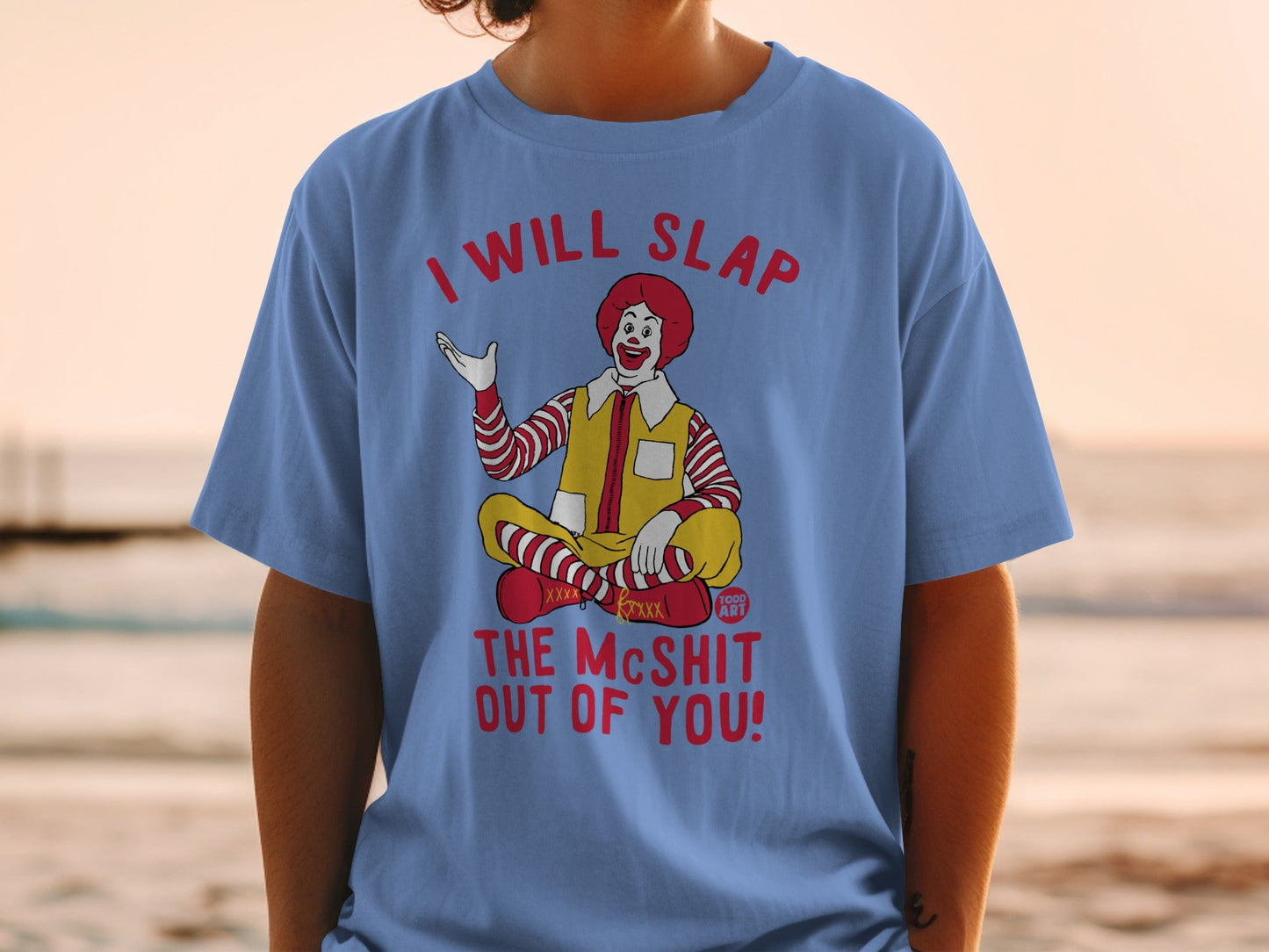 Ronald McDonald sitting cross-legged, wearing a shirt that says "I will slap the mcshit out of you!".