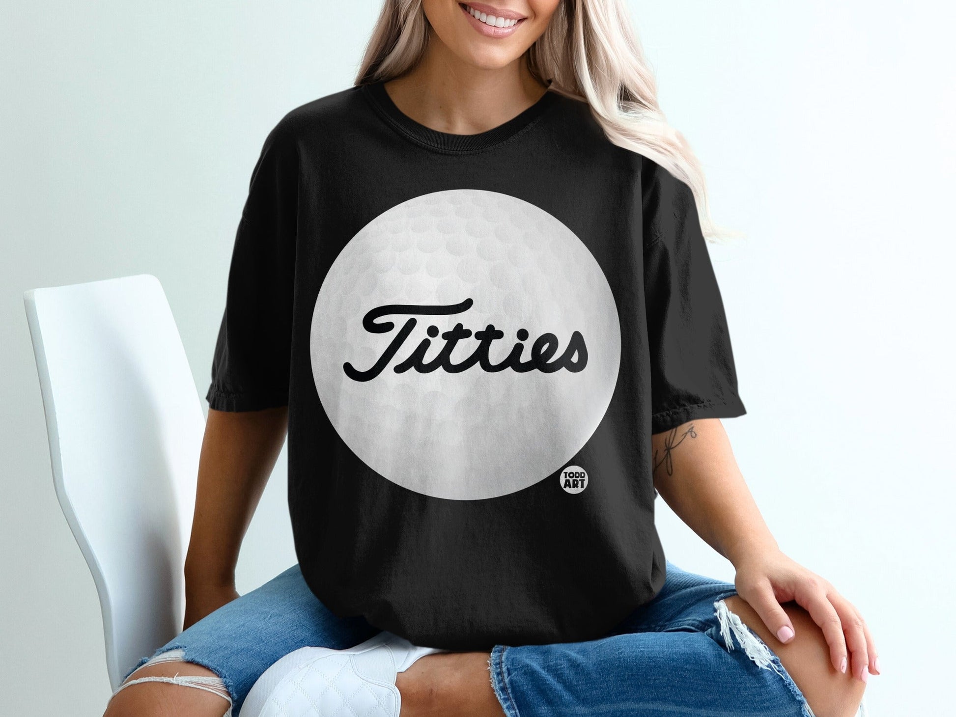Black t-shirt with a large white golf ball and the word "Titties" in cursive.