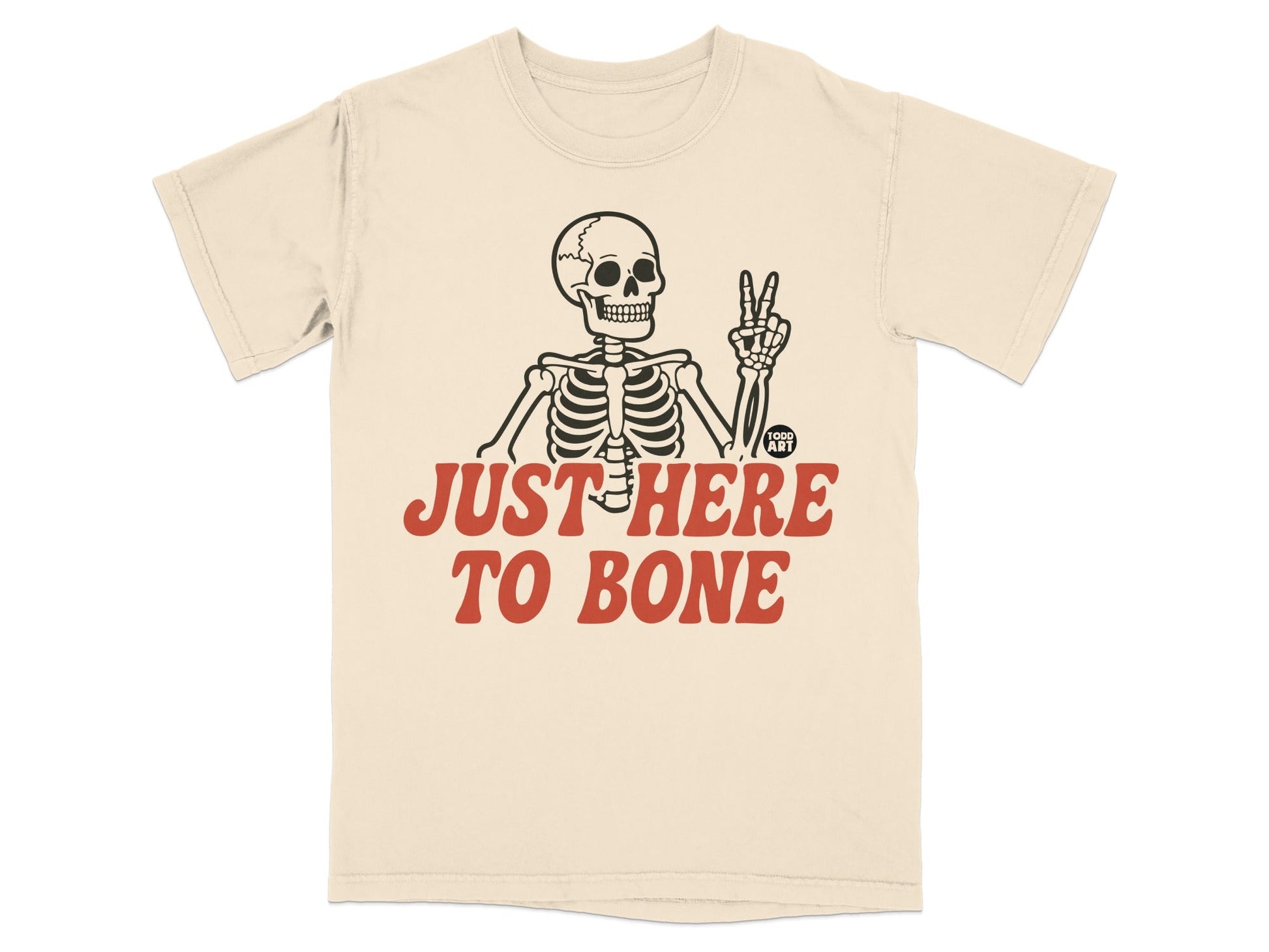 Cream t-shirt with skeleton giving peace sign and text "JUST HERE TO BONE".