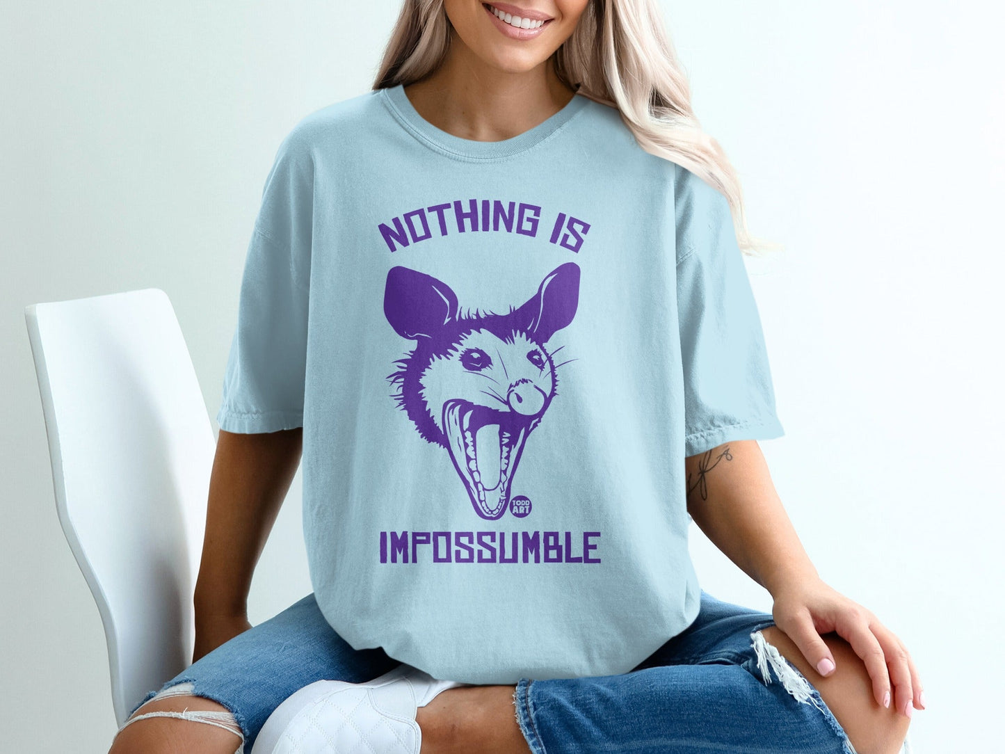 Light blue t-shirt with purple opossum graphic and text "NOTHING IS IMPOSSUMBLE".