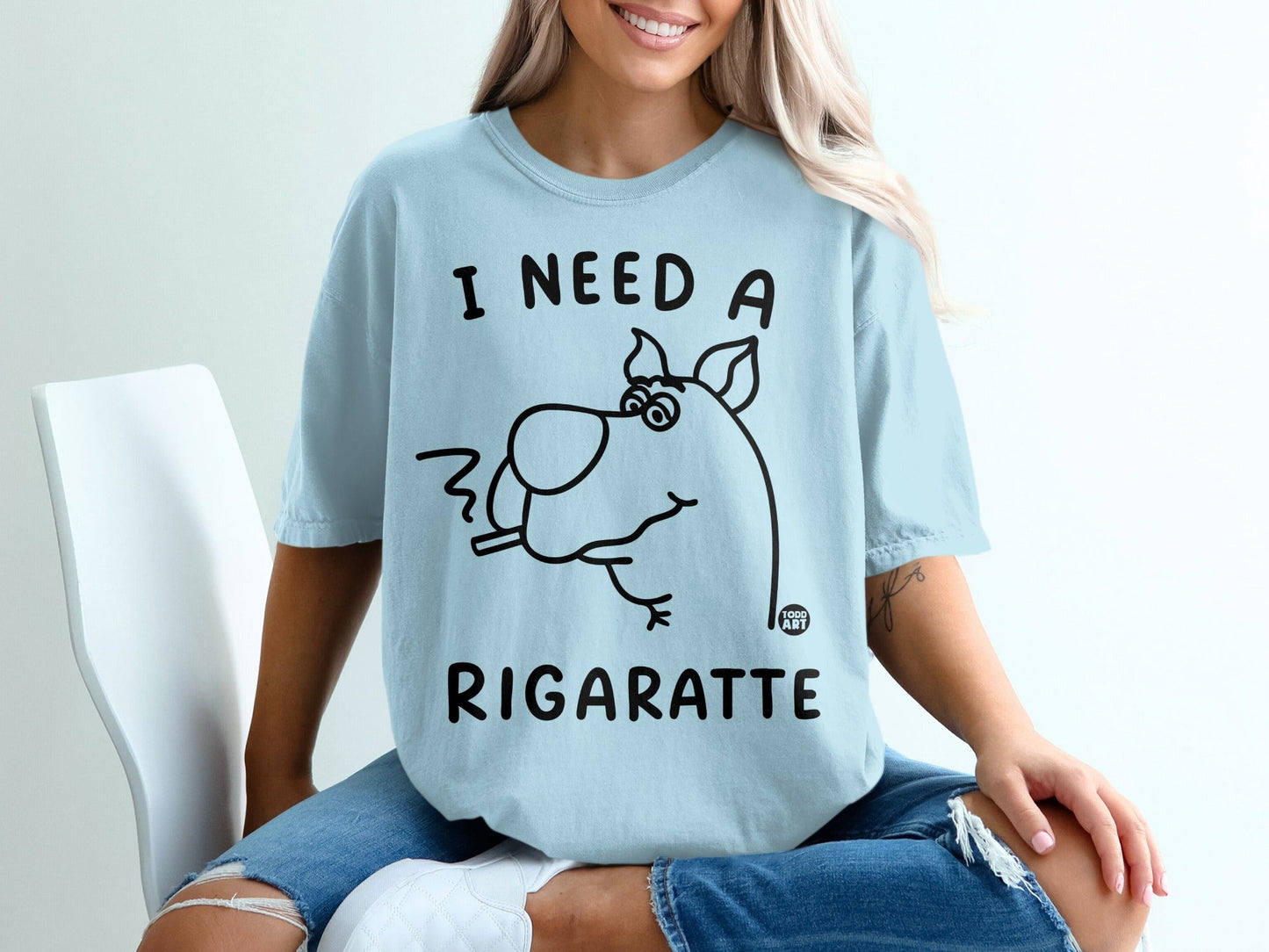 Light blue t-shirt with cartoon dog smoking a cigarette, reads "I need a rigarette".