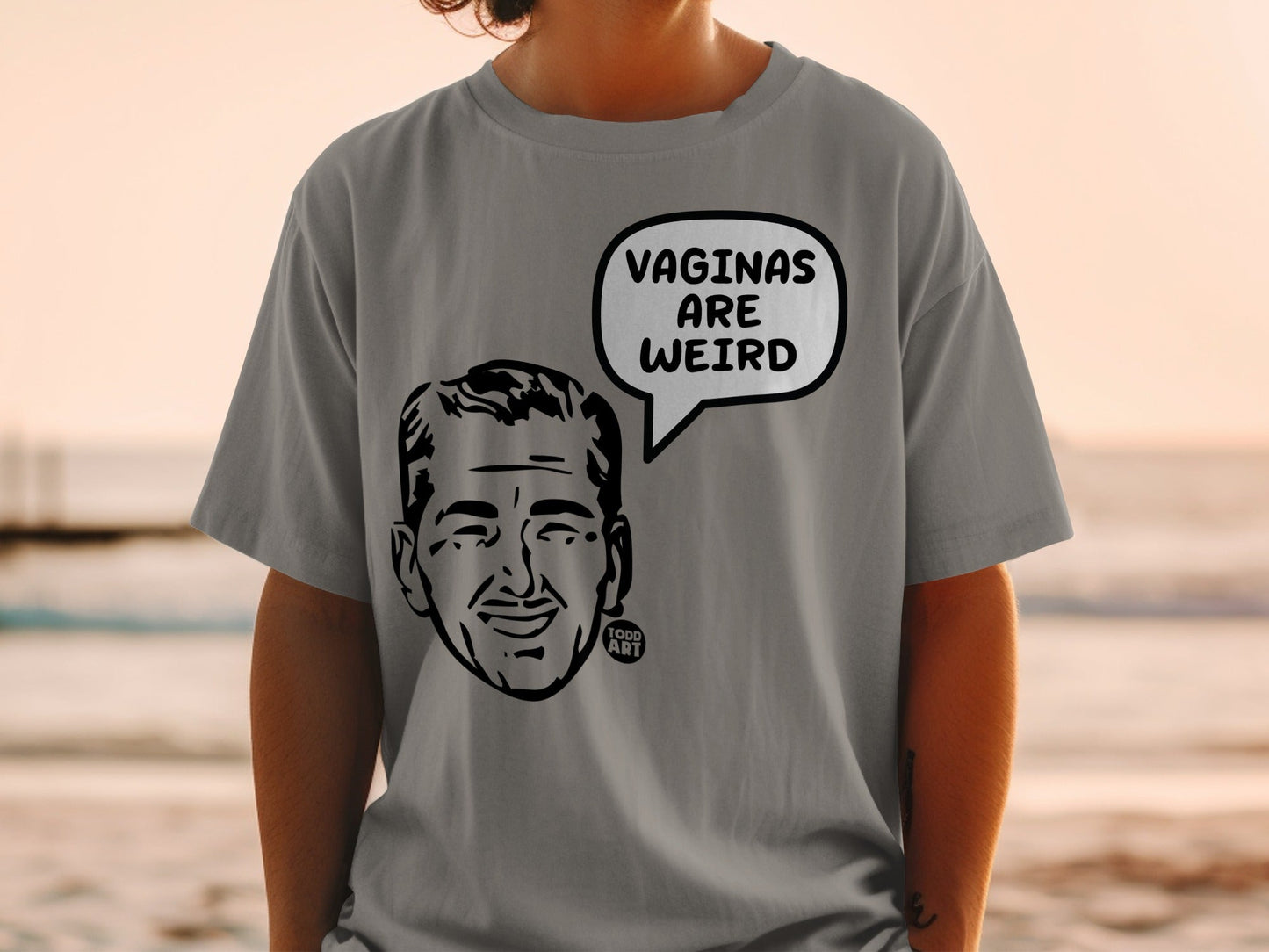 Grey t-shirt with black graphic of a man's face and "VAGINAS ARE WEIRD" speech bubble.