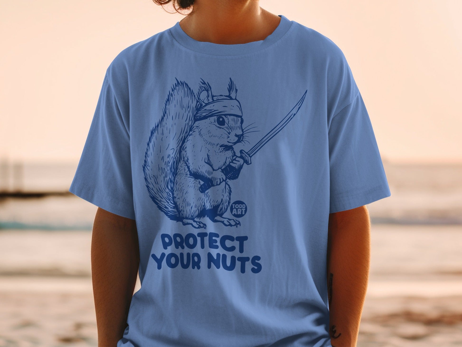 Blue t-shirt with a squirrel holding a sword, text "PROTECT YOUR NUTS".