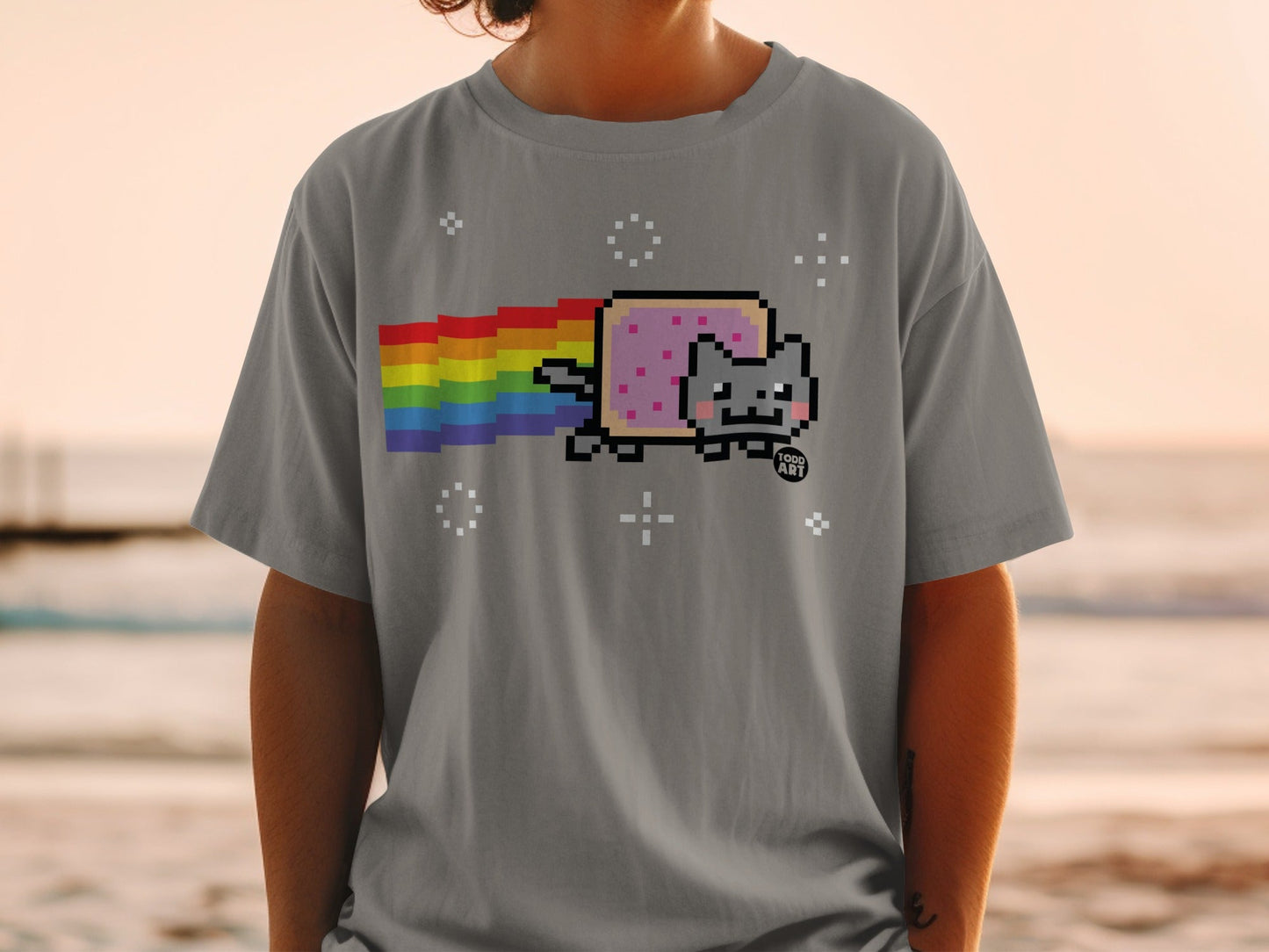 Pixelated cat with rainbow trail on gray t-shirt.