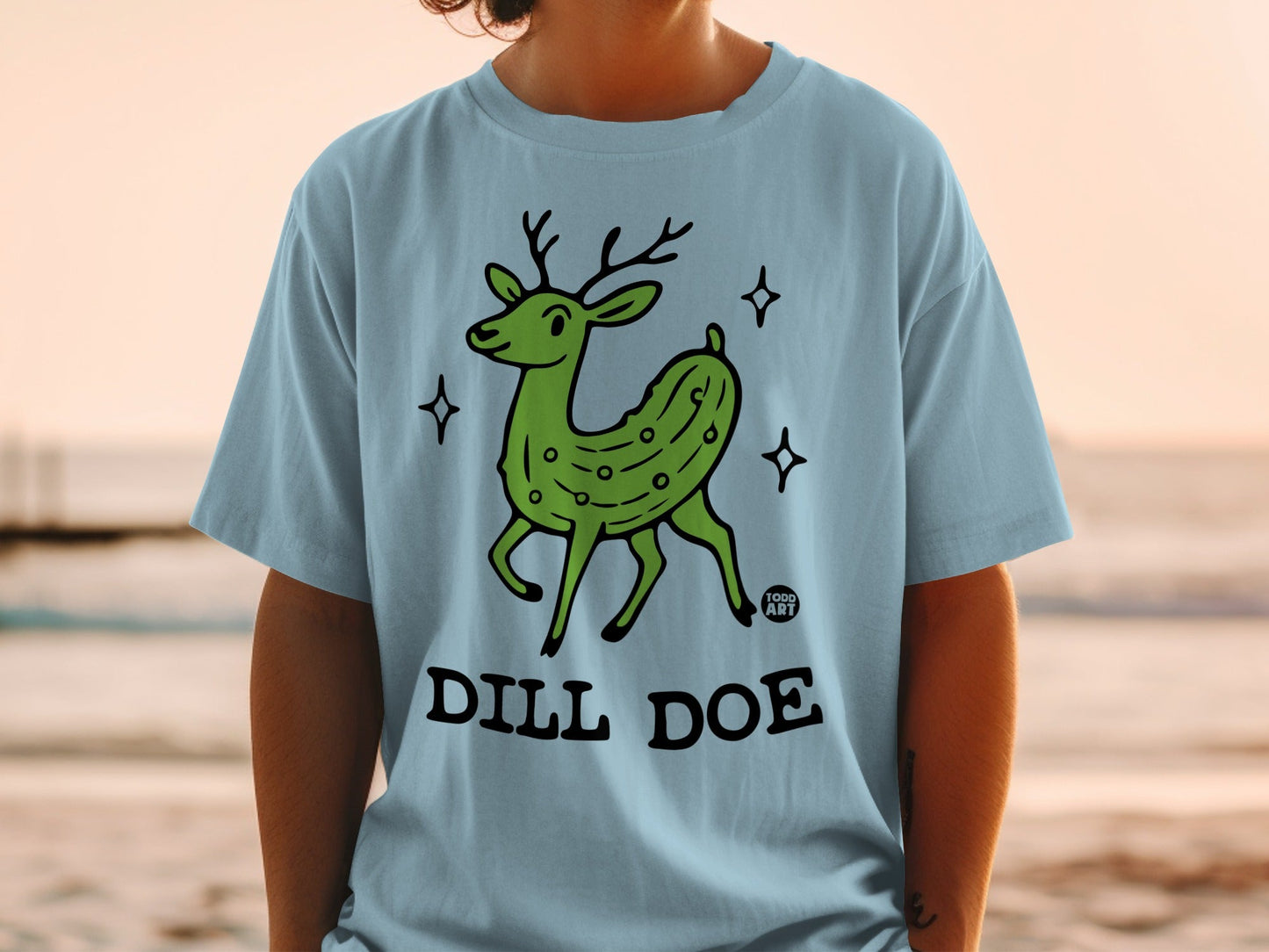 Green dill pickle deer with "DILL DOE" text on a light blue t-shirt.