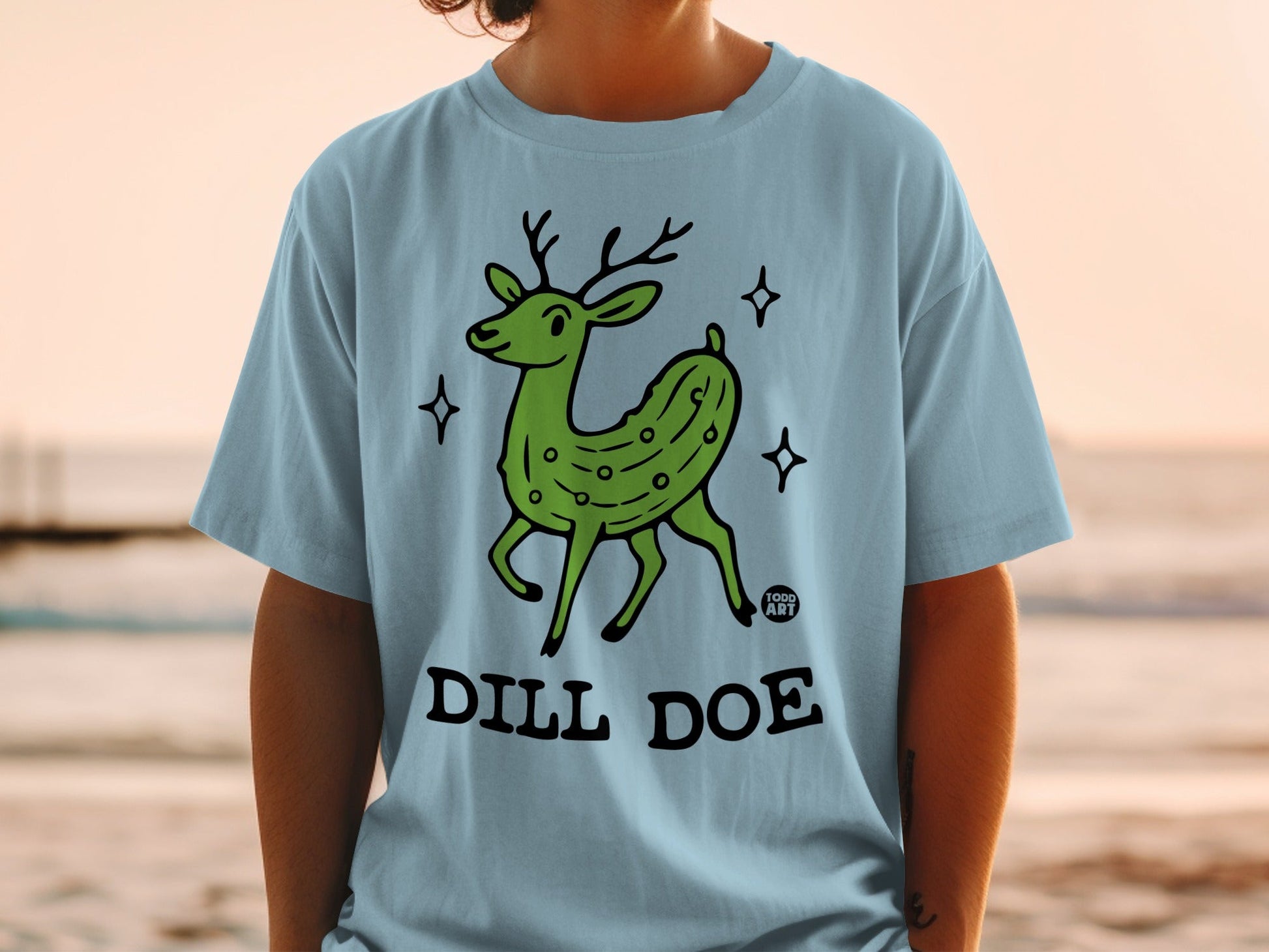 Green dill pickle deer with "DILL DOE" text on a light blue t-shirt.