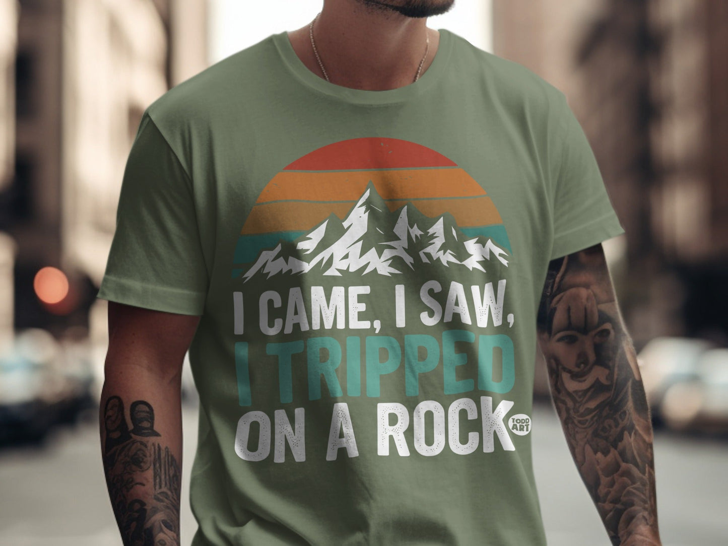 Green t-shirt with mountain sunset graphic and "I came, I saw, I tripped on a rock" text.