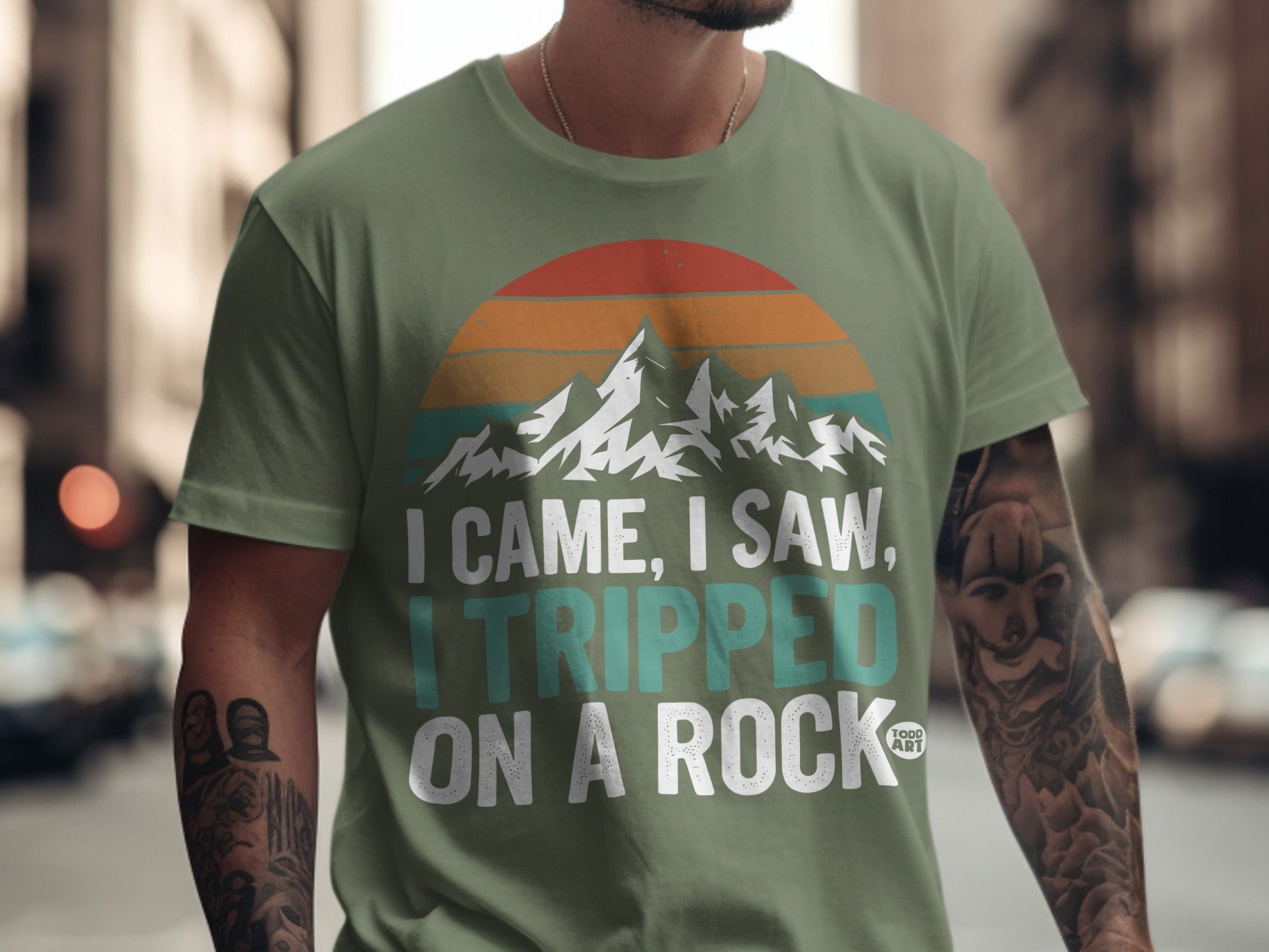 Green t-shirt with mountain sunset graphic and "I came, I saw, I tripped on a rock" text.