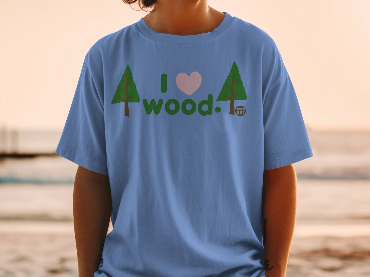 Light blue t-shirt with green trees, pink heart, and "I love wood" text.