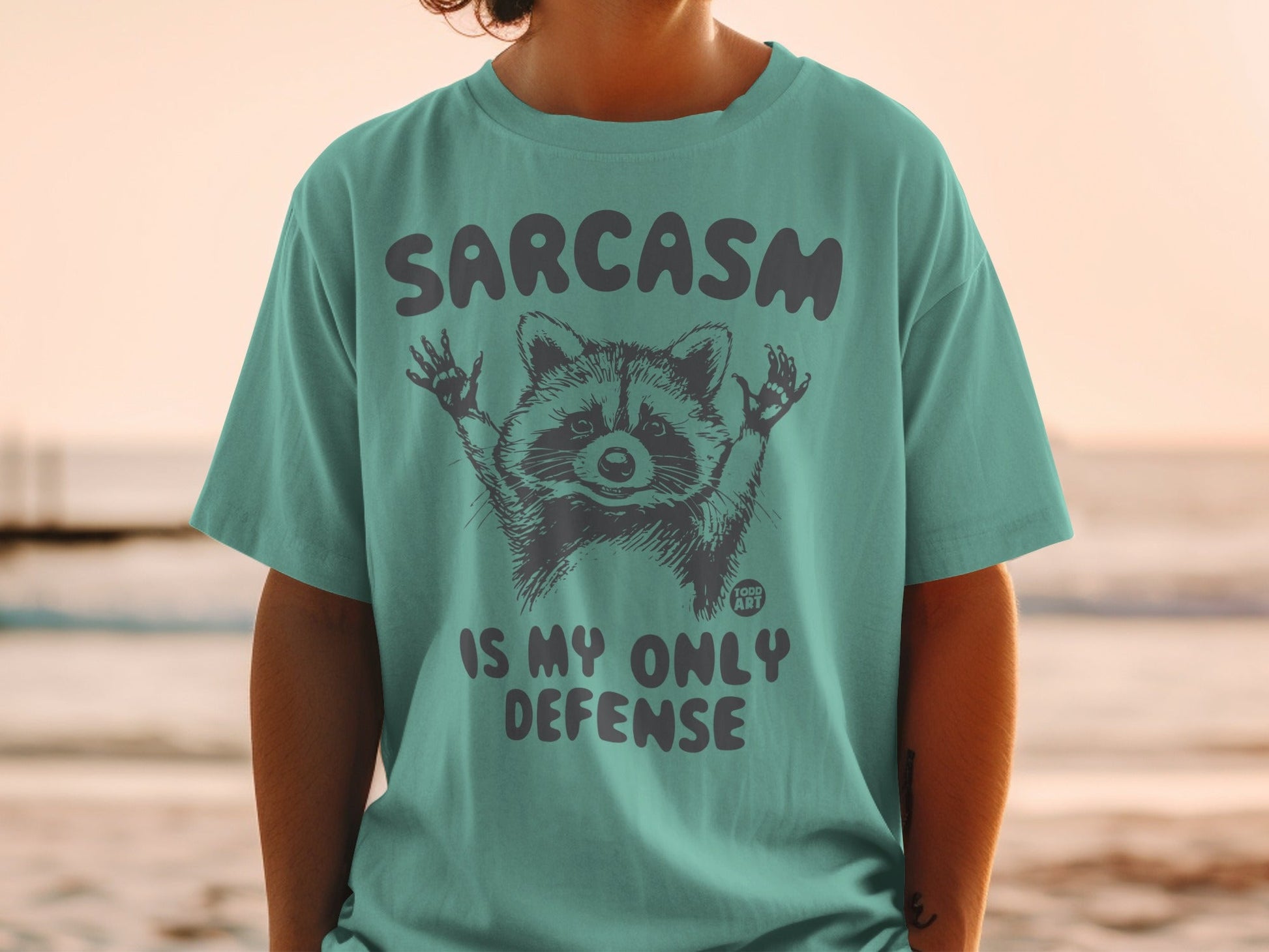 T-shirt with raccoon graphic and text "Sarcasm is my only defense."